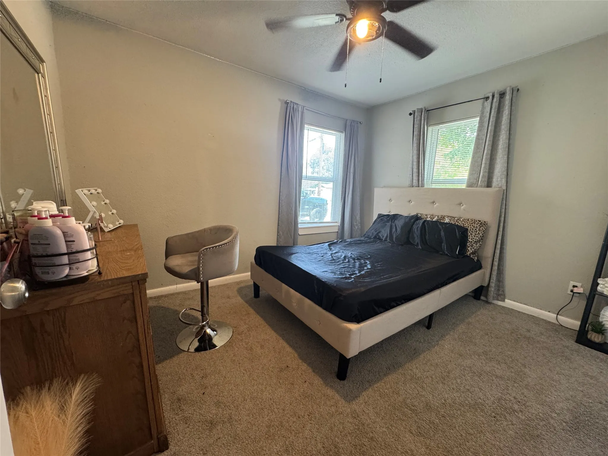 Carpeted bedroom featuring two windows with draperies, a ceiling fan with integrated lighting, and a neutral wall color