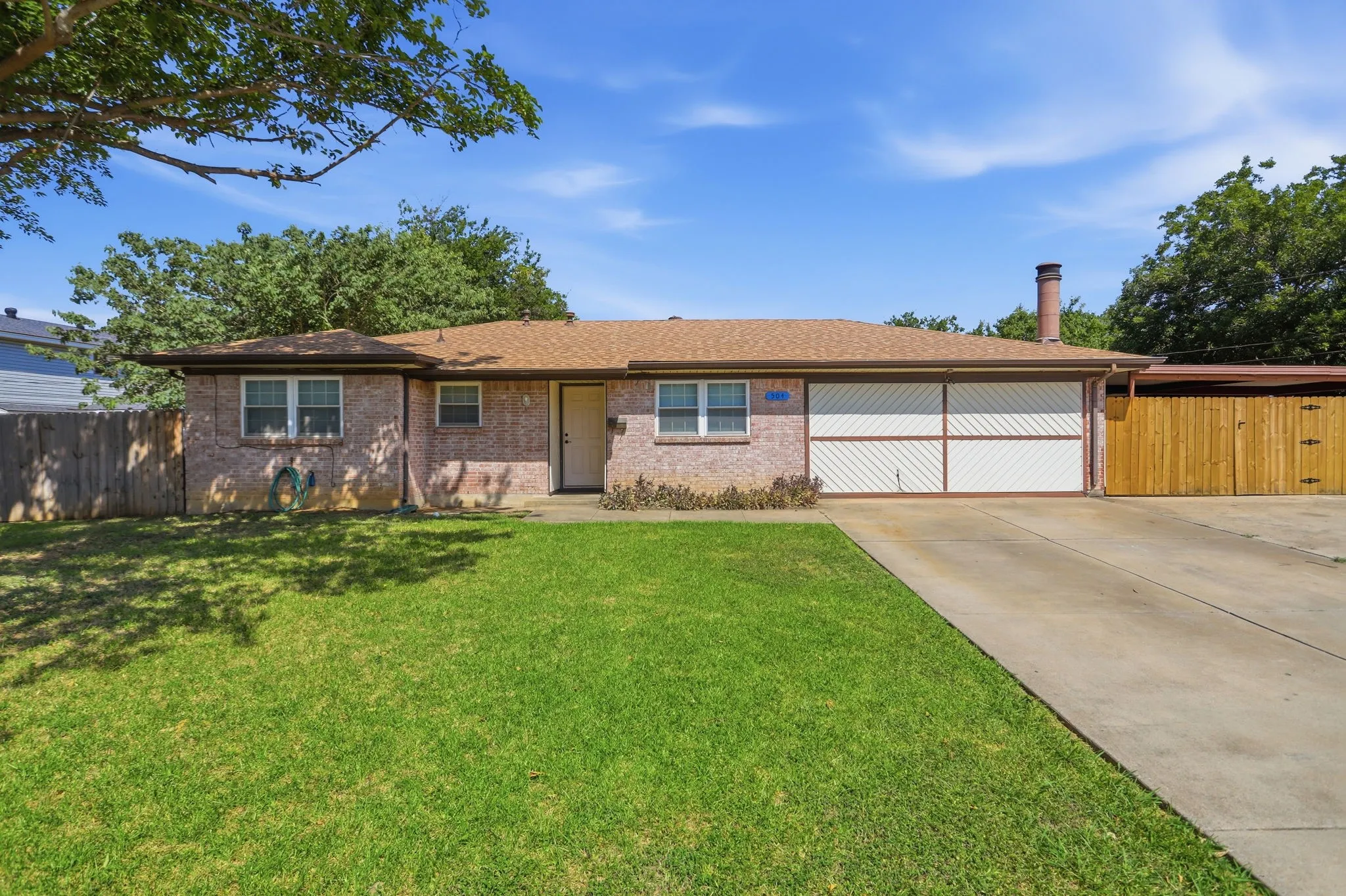 Brick exterior with a brown shingle roof, attached garage featuring a white door with diagonal accents, and a concrete driveway