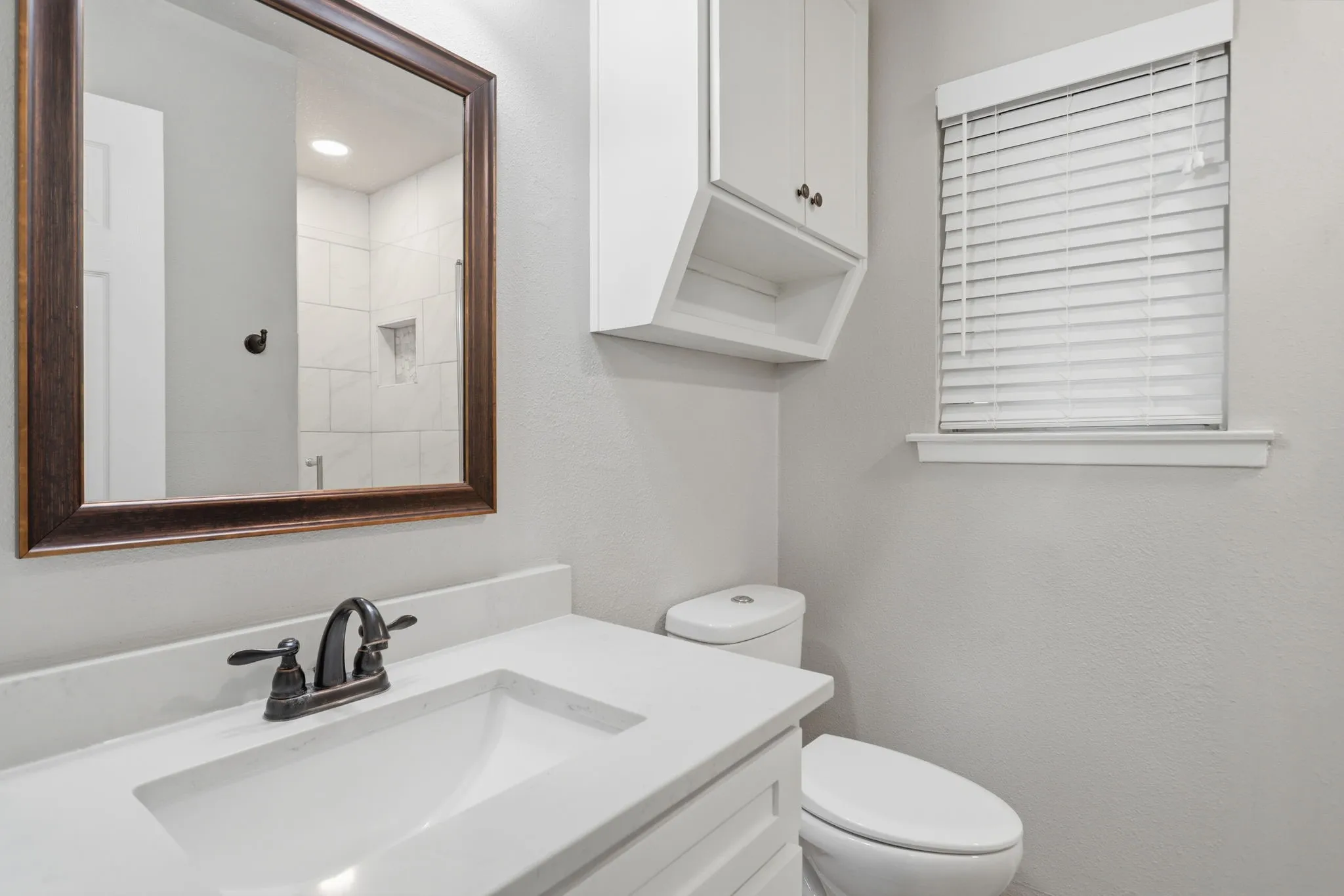 Bathroom vanity with an integrated white sink, bronze-finish faucet, and coordinating framed mirror