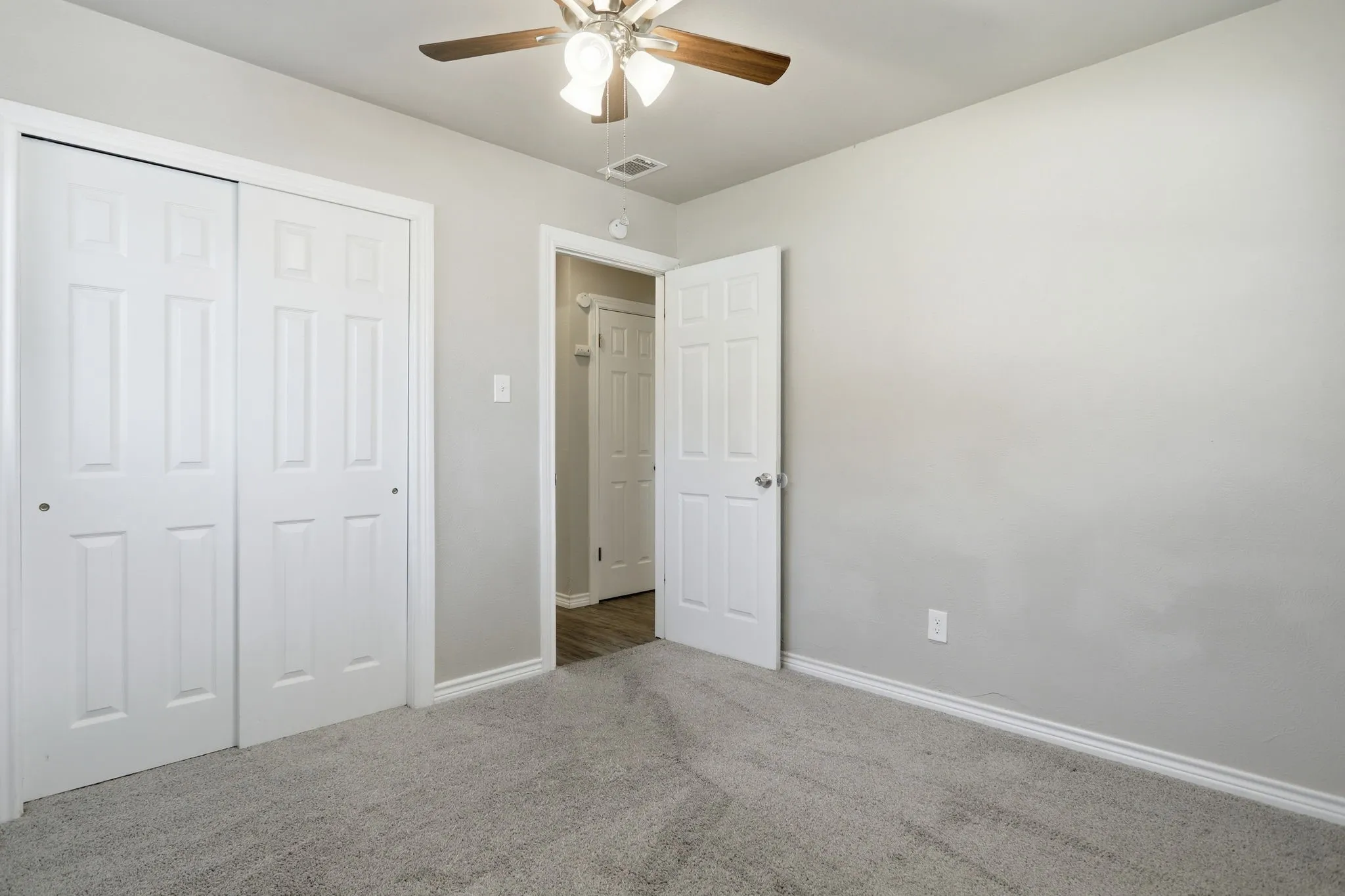 Room featuring light gray wall paint, gray carpeting, a multi-paneled white door, and a ceiling fan with light fixture
