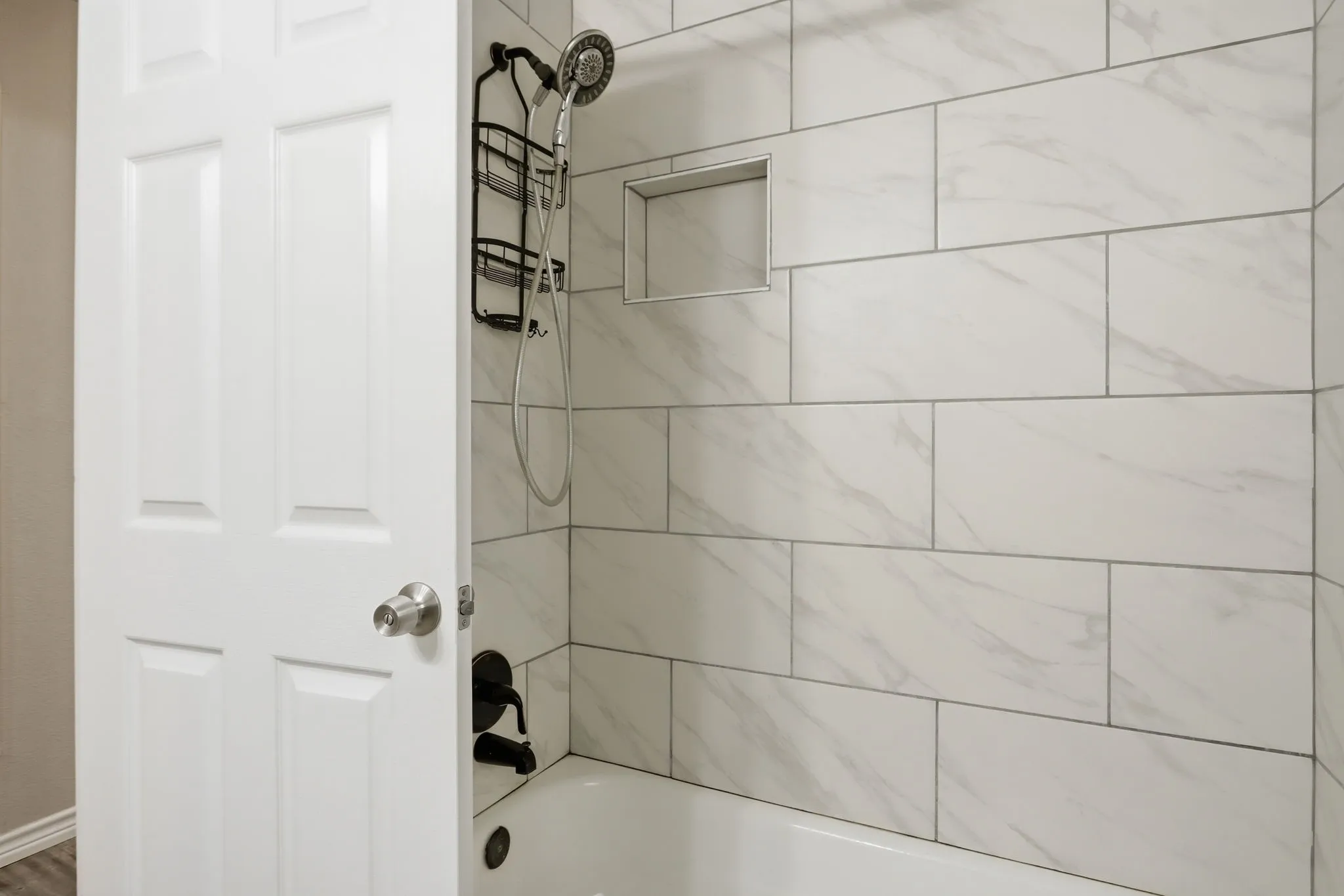 Tub/shower combination featuring white subway tile surround with subtle veining and a recessed niche