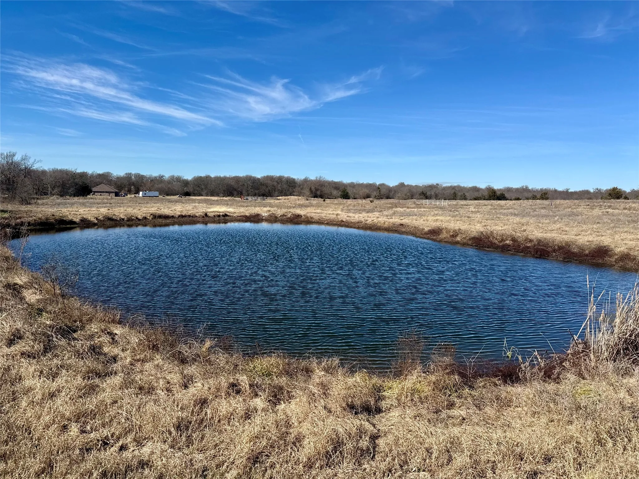 Reflective pond with natural banks, surrounded by expansive grassland
