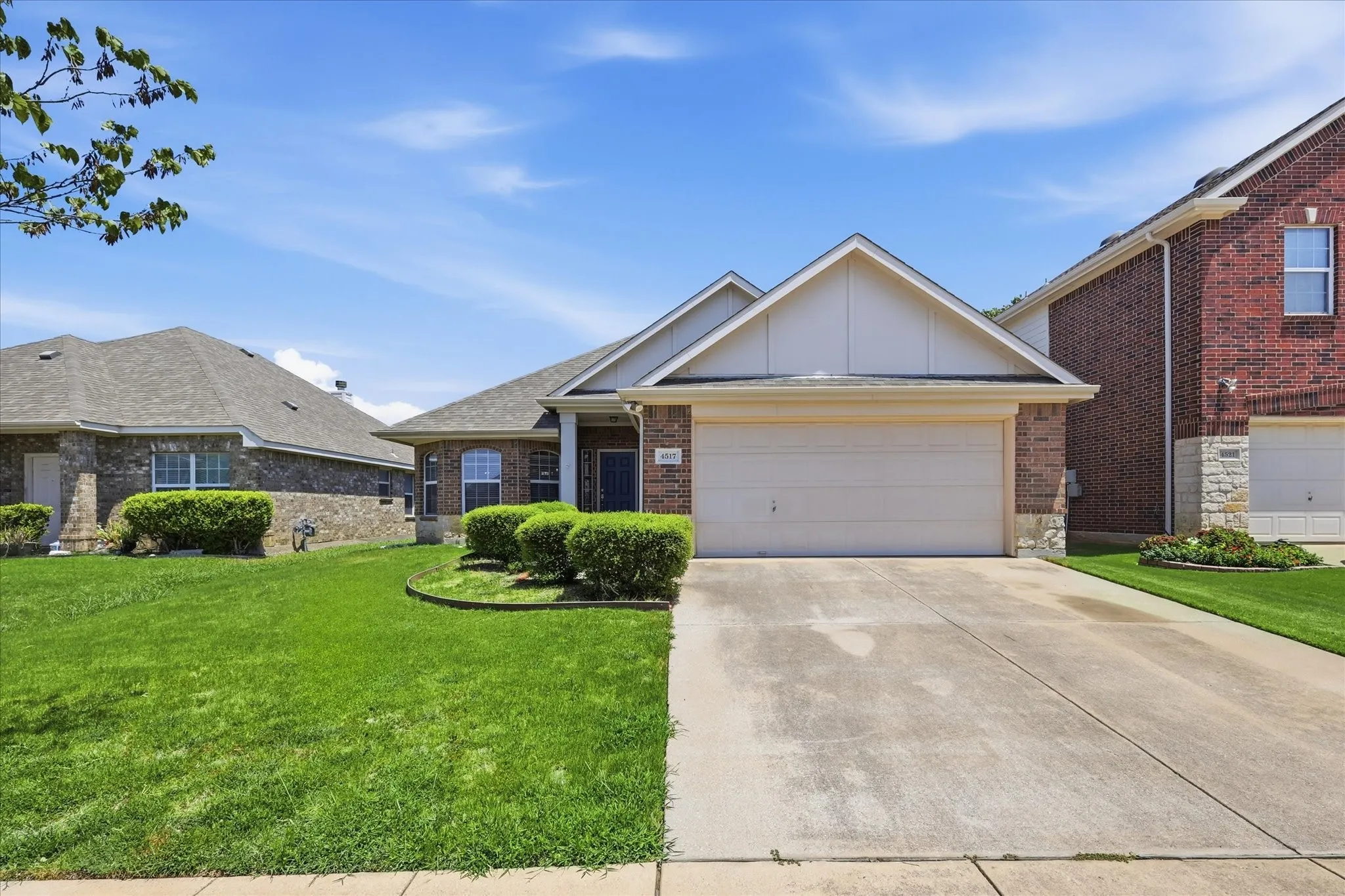 Brick and stone facade residence featuring a two-car garage, concrete driveway, and front lawn with established landscaping