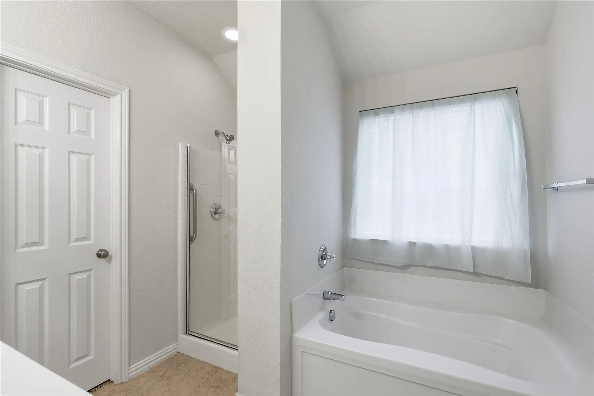 White soaking tub with chrome fixtures and an adjacent glass-enclosed shower with tile surround