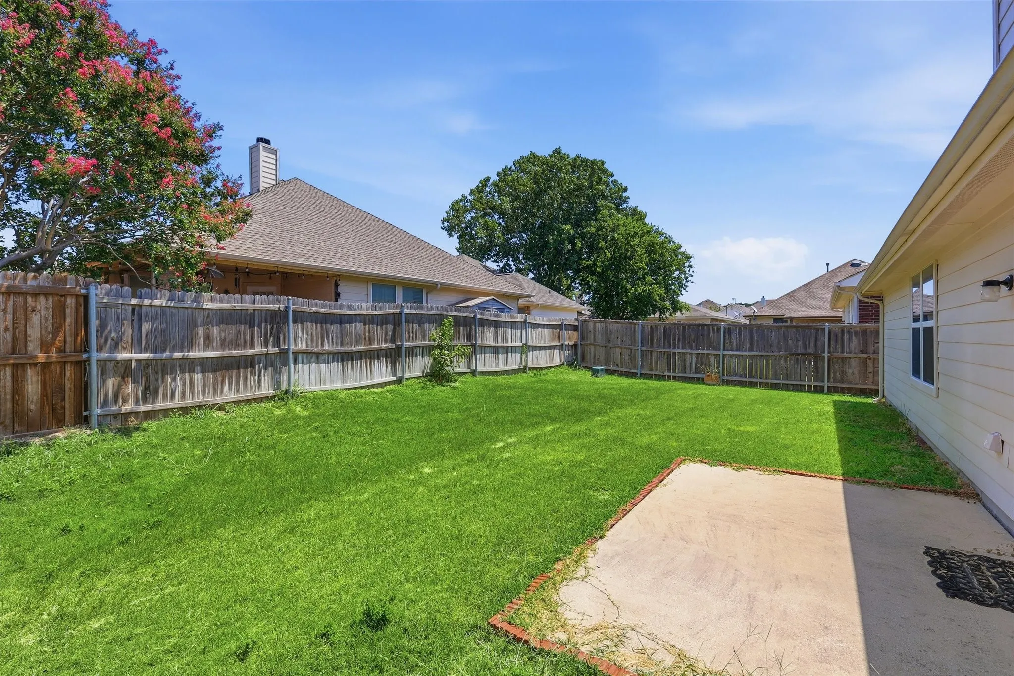 Expansive backyard featuring a concrete patio, wood fencing, and a manicured lawn