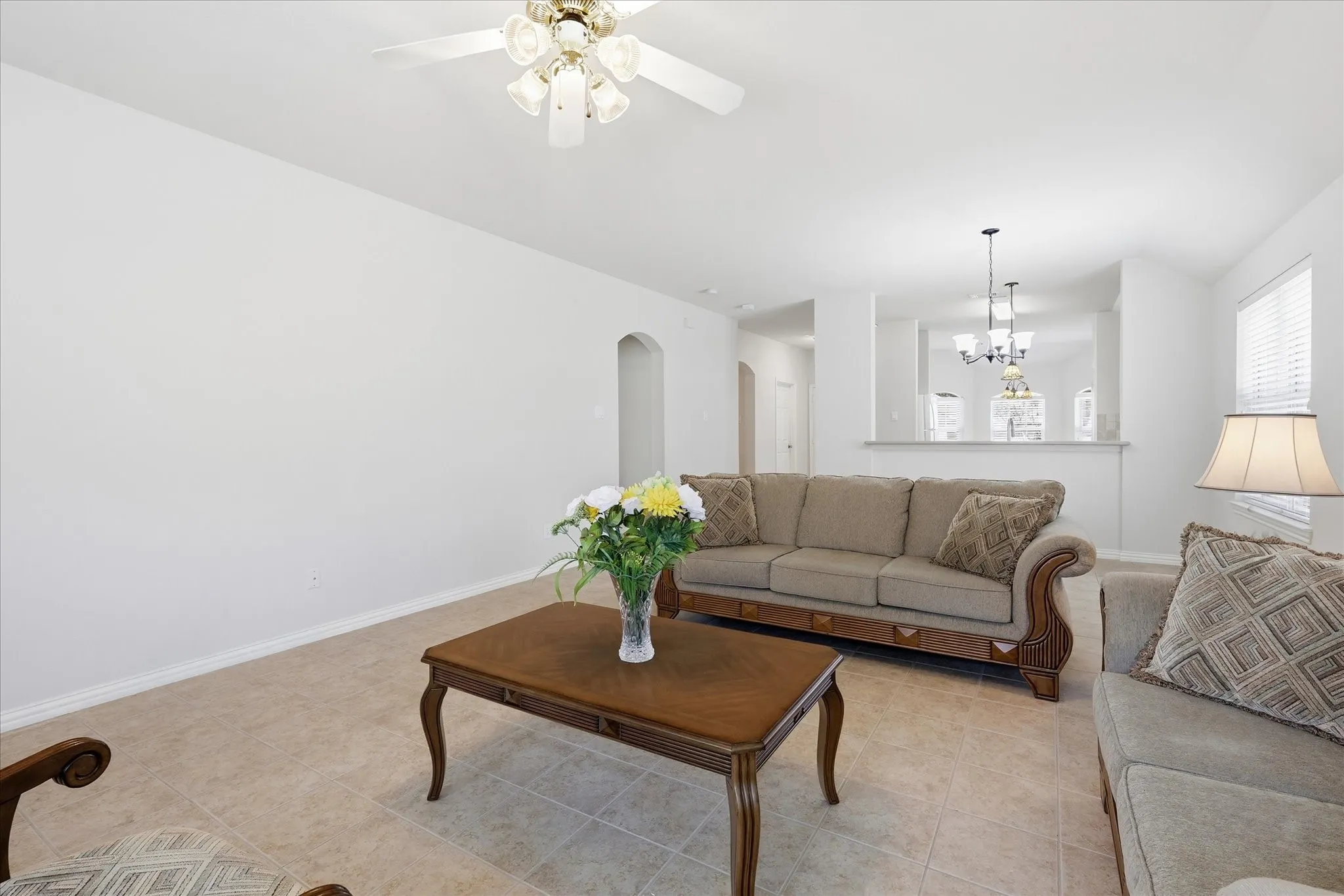 Living area featuring tile flooring, a ceiling fan with integrated lighting, and an arched doorway