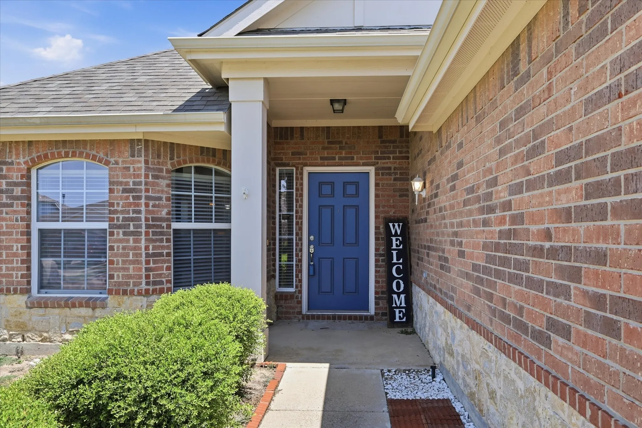 Brick exterior with stone accents, featuring an arched window design and a blue panel front door