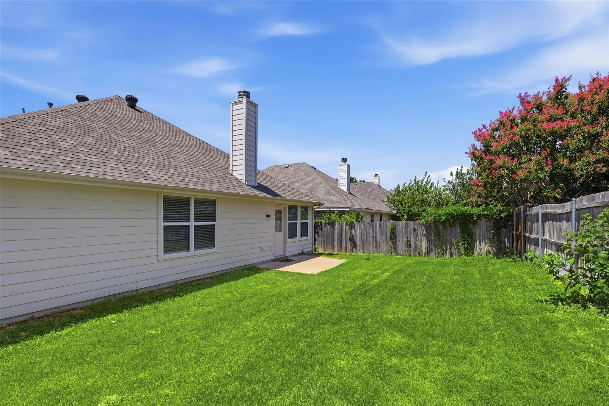 Expansive backyard featuring a large green lawn, concrete patio, and mature landscaping