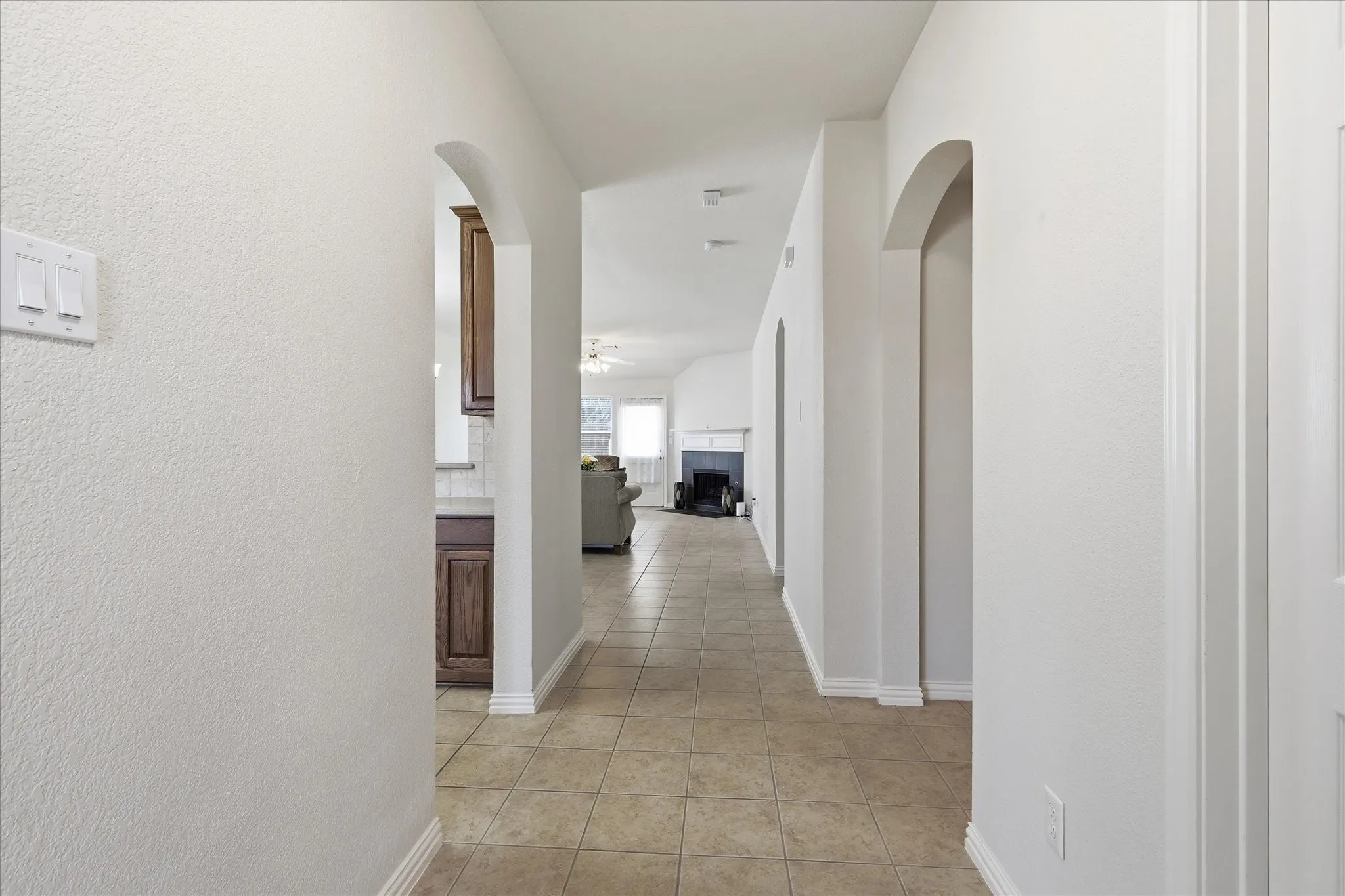 Archway entryways define the hallway, featuring light-colored square floor tiles