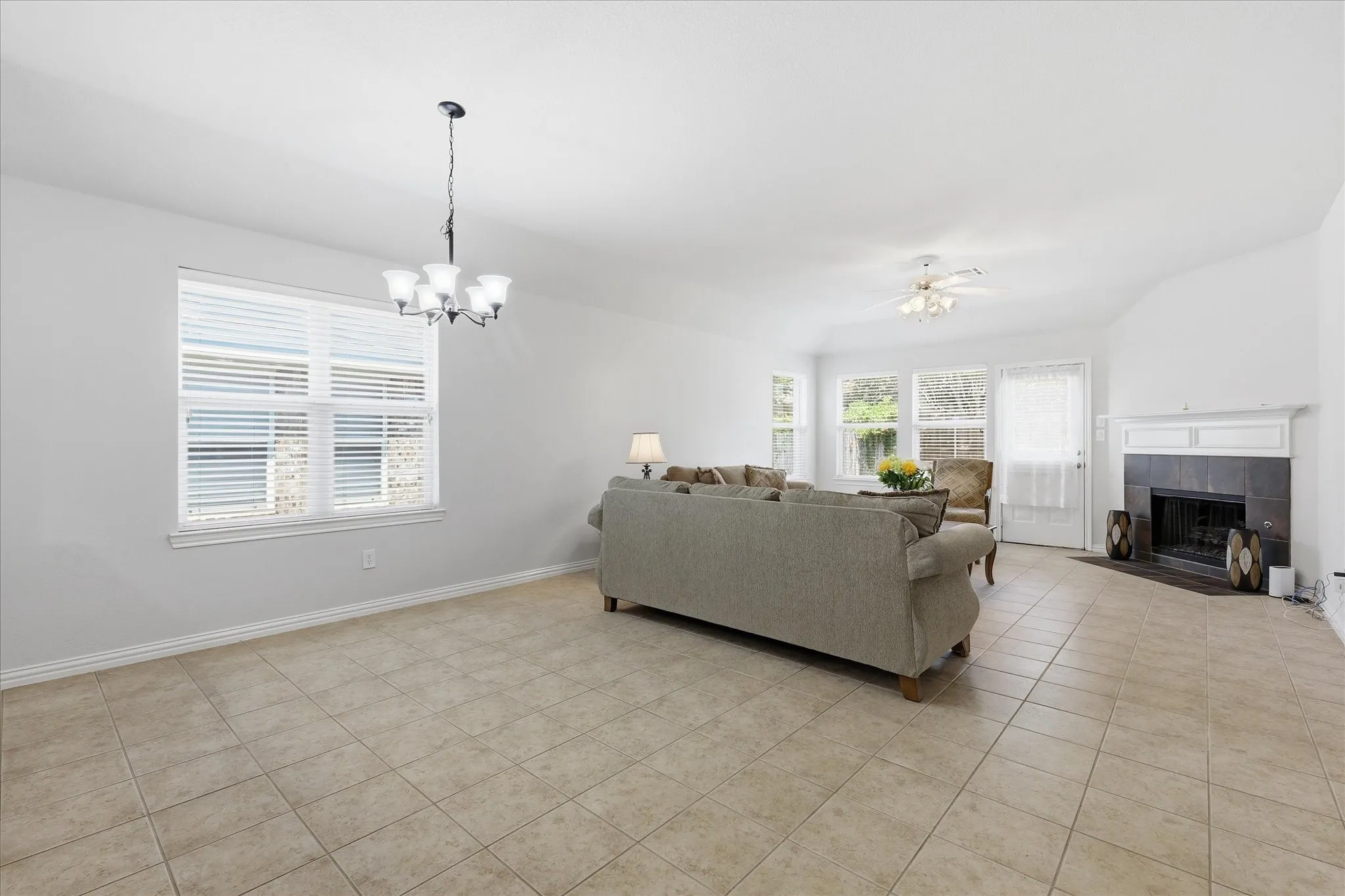 Spacious living area featuring light-toned tile flooring, multiple windows with blinds, and a white ceiling fan