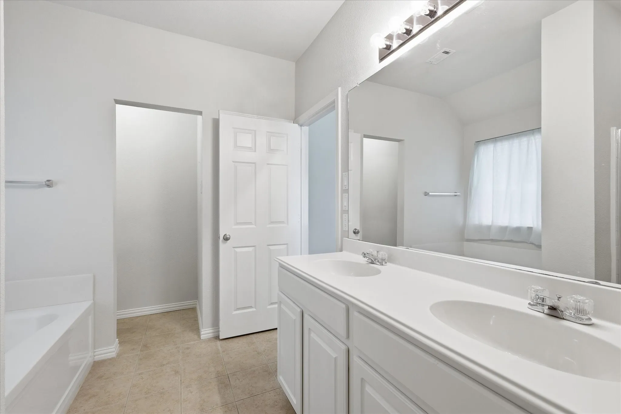 Bathroom featuring a dual vanity with integrated sinks, a built-in bathtub, a large wall-mounted mirror, and tile flooring