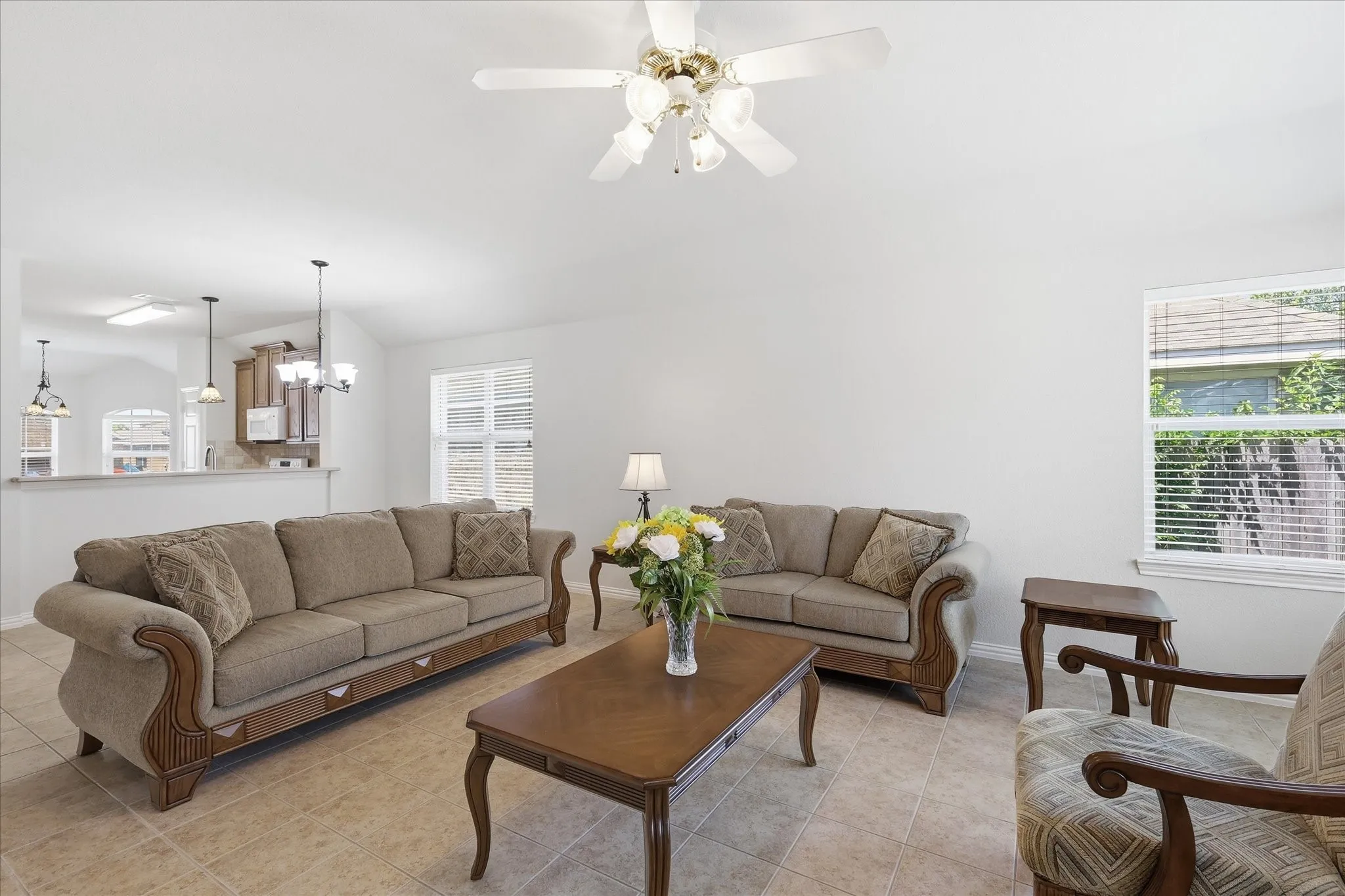 Spacious living area featuring tile flooring, a ceiling fan with integrated lighting, and multiple windows with blinds