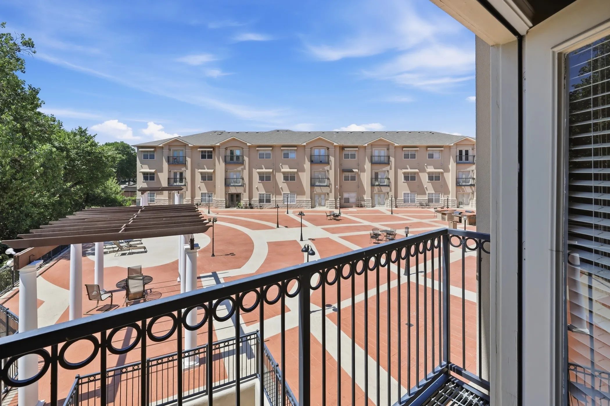 Balcony with wrought iron railing overlooking a communal courtyard with patterned red and beige hardscaping