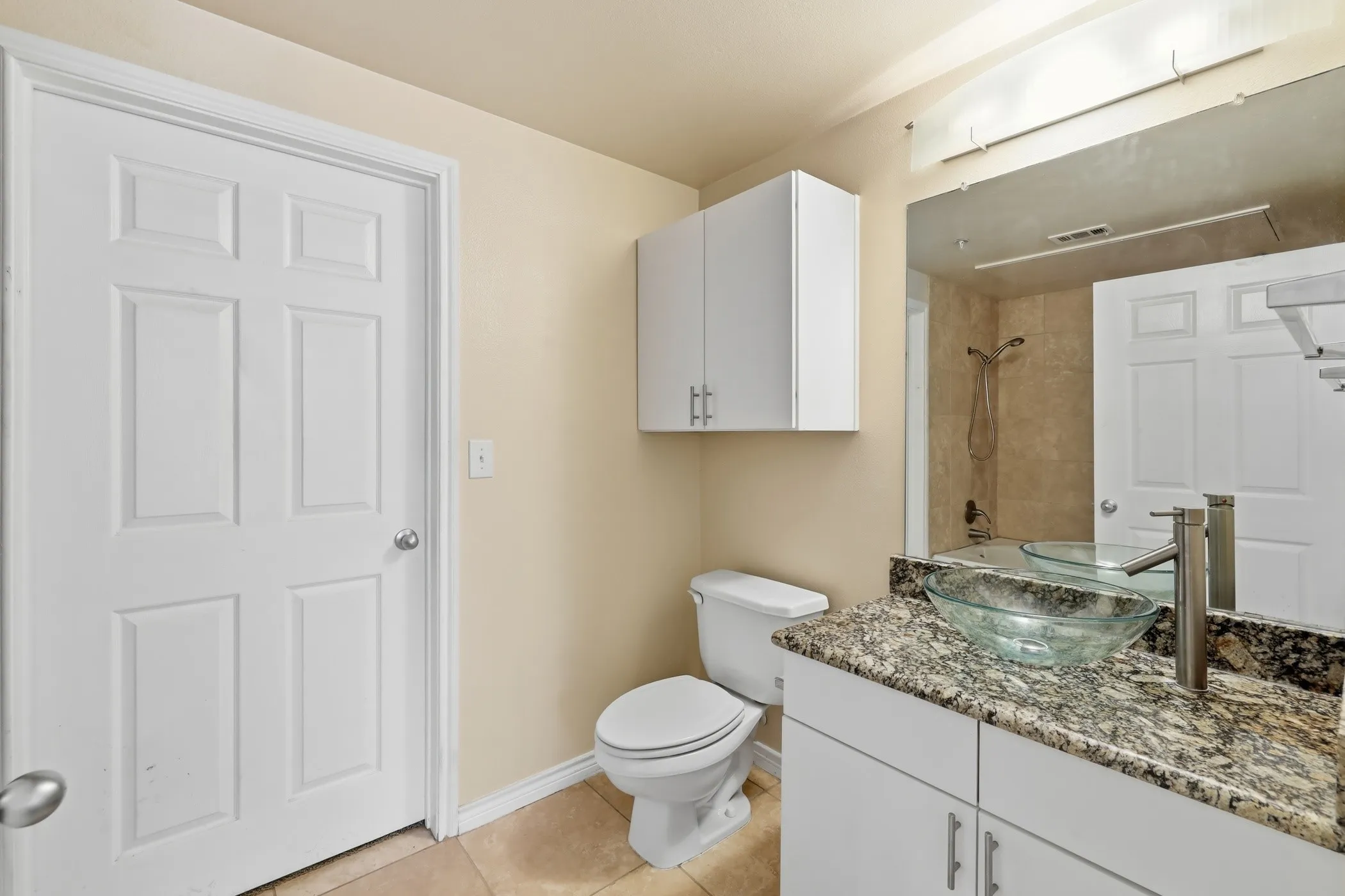 Modern bathroom featuring a granite countertop vanity with a glass vessel sink, brushed nickel faucet, and white cabinetry