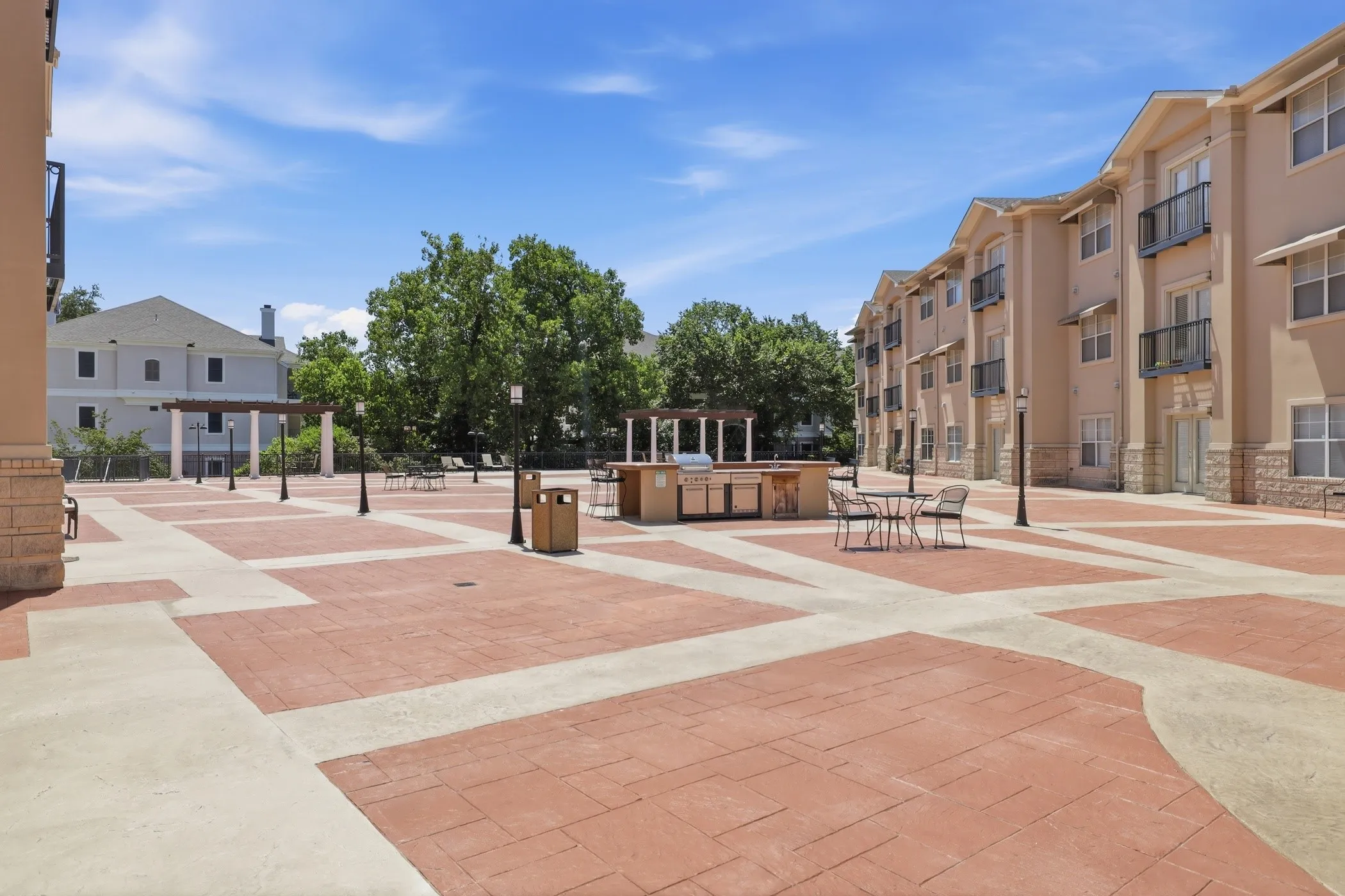 Expansive outdoor patio area featuring a paver and concrete surface, an outdoor grilling station with built-in cabinetry, multiple pergolas, and lampposts