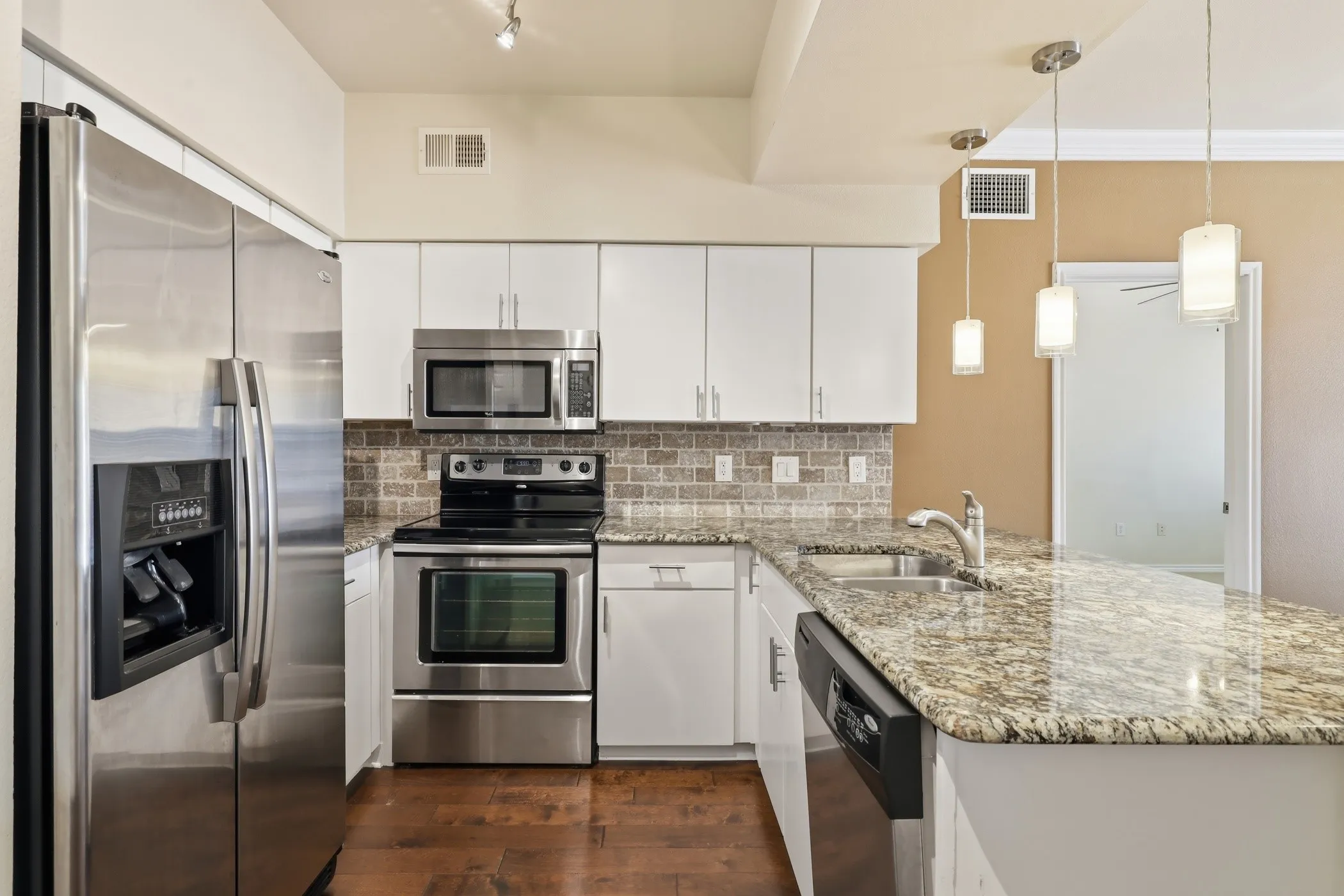 Modern kitchen featuring stainless steel appliances, granite countertops, white cabinetry, a tile backsplash, and wood-finish flooring