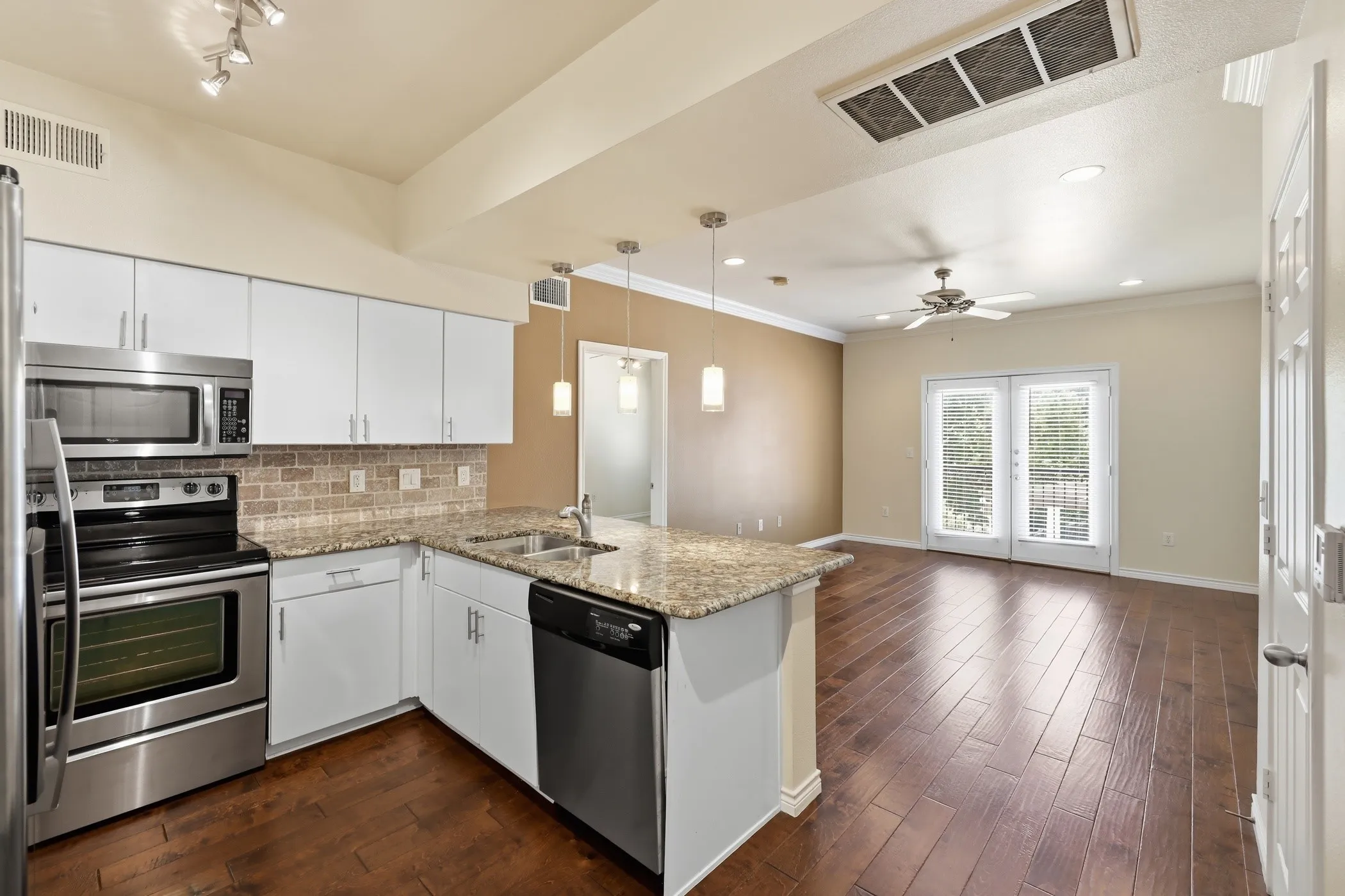 Open-concept living space featuring wood-finish flooring, a kitchen island with stone countertops, stainless steel appliances, and white cabinetry