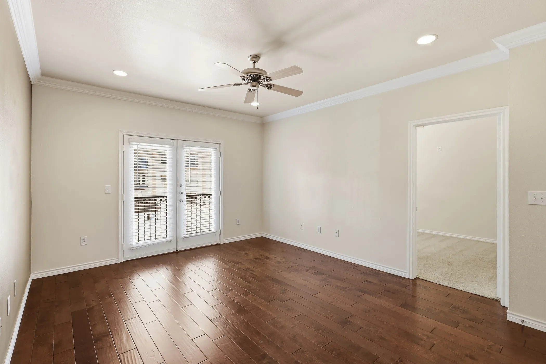 Spacious room with wood-finish flooring, French doors opening to a balcony with iron railings, crown molding, a ceiling fan, and recessed lighting