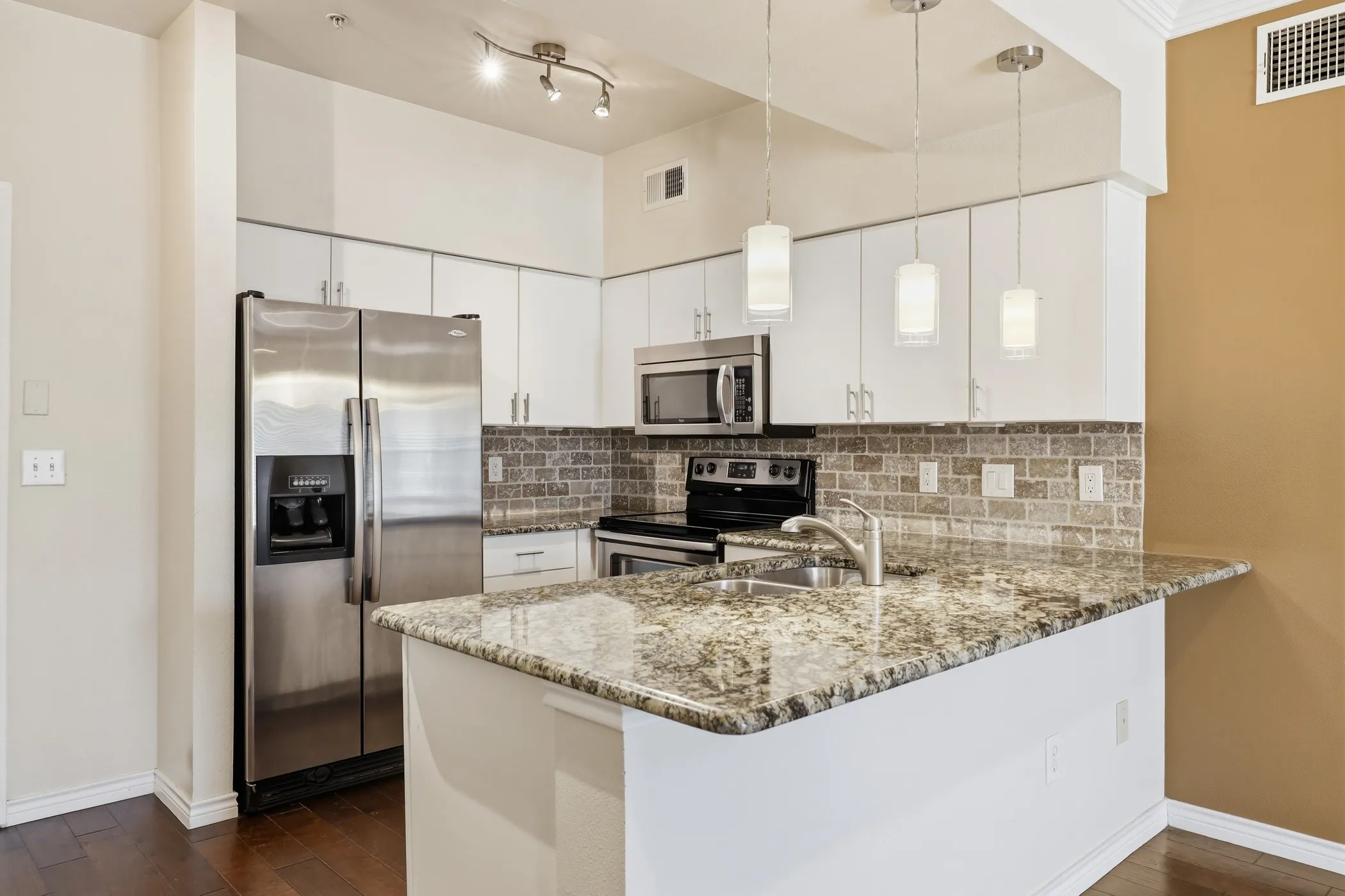 Kitchen featuring white cabinetry, stainless steel appliances, a stone countertop island with integrated sink, a tiled backsplash, and wood-finish flooring