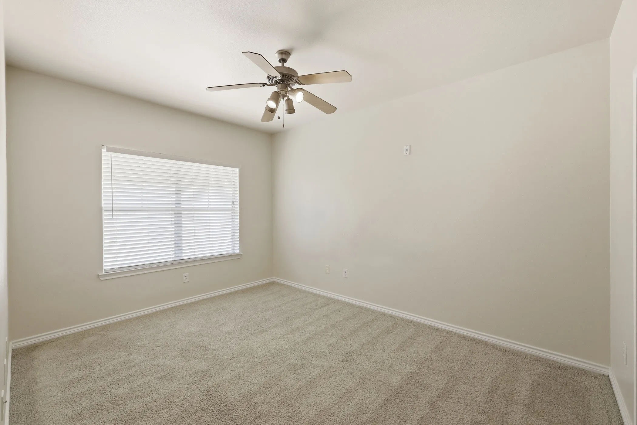 Carpeted interior room featuring a window with horizontal blinds, a ceiling fan with integrated lighting, neutral wall paint, and white baseboards