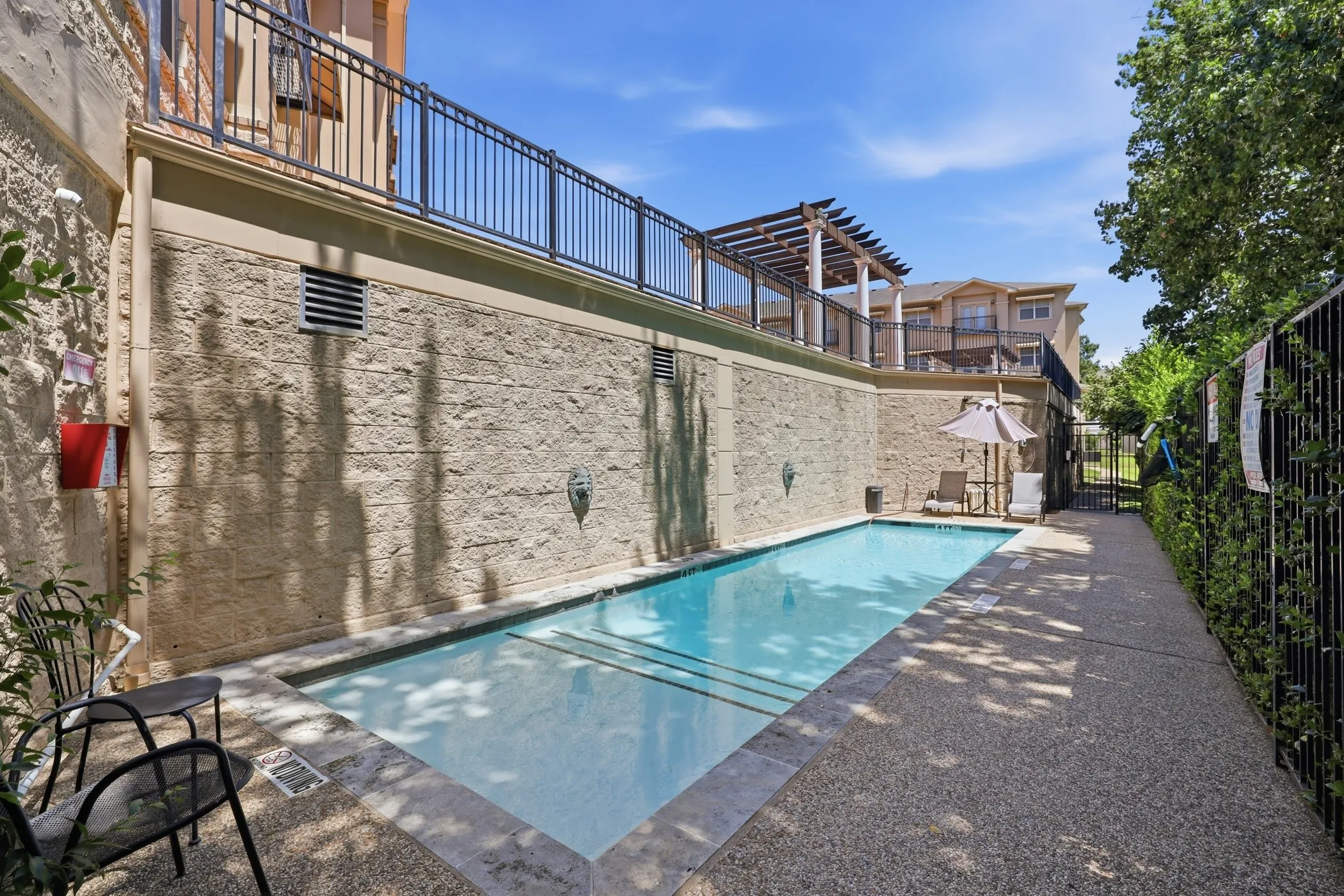 Outdoor swimming pool with tiled coping, stone-textured retaining wall, and metal railing