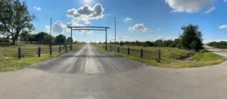 Paved entrance to the property, featuring a metal archway and perimeter fencing