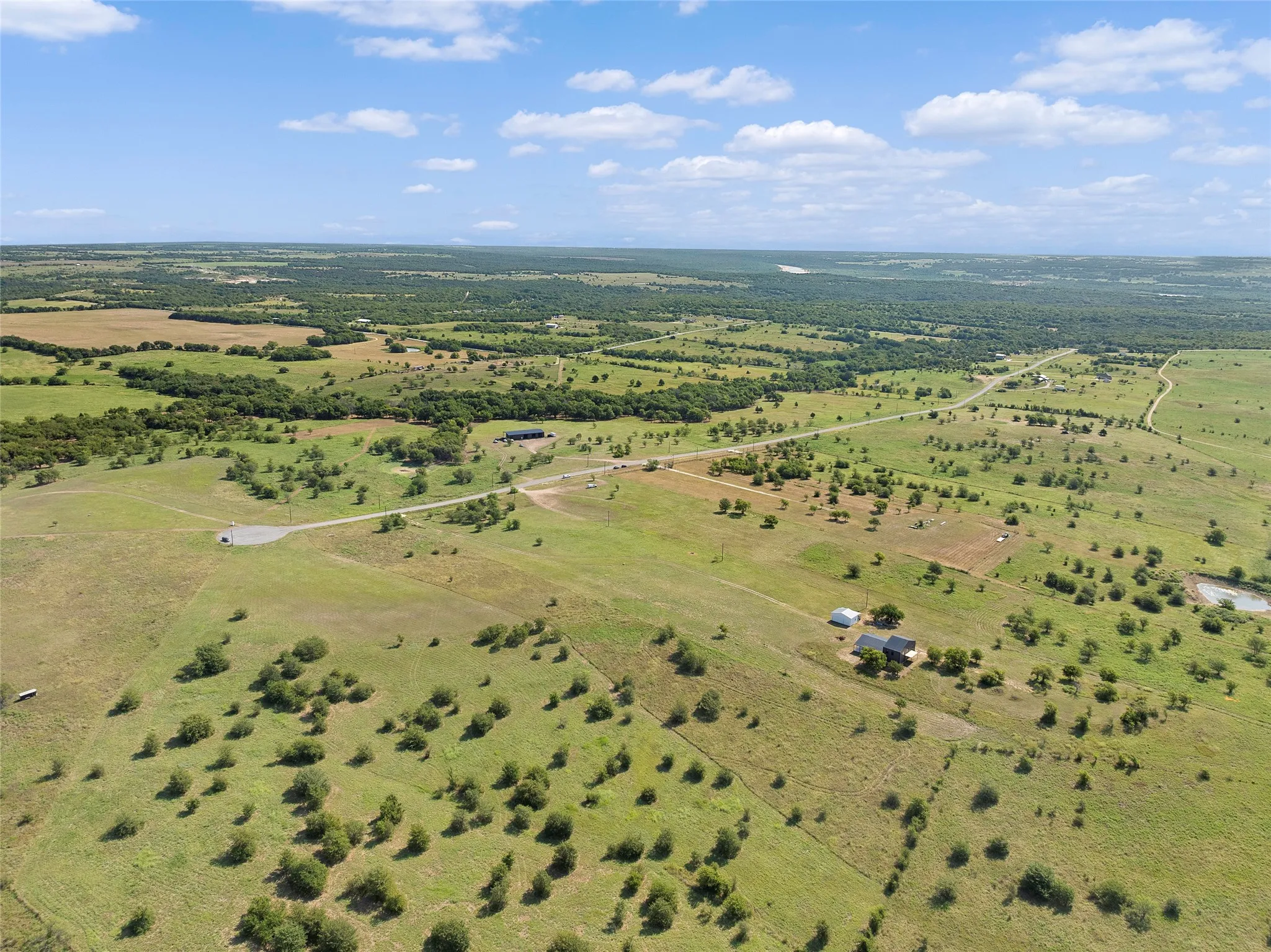 Expansive rural landscape featuring green pastures, scattered trees, and a distant road