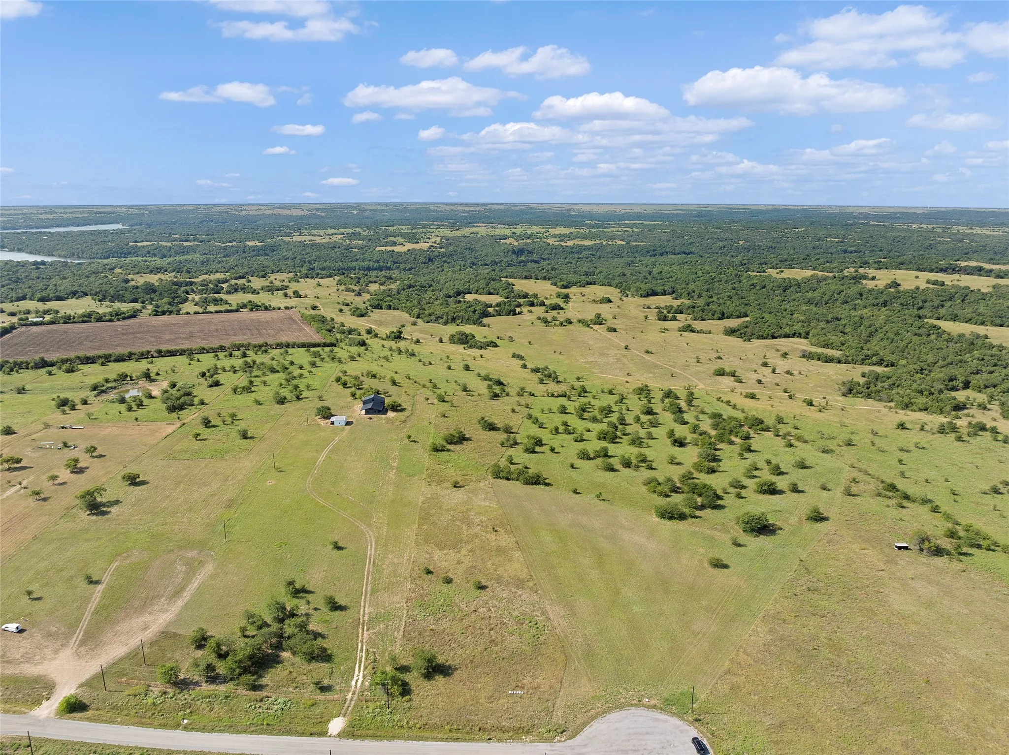 Expansive rural landscape featuring a single-story dwelling, cultivated land, and mature tree lines