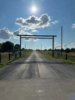 Paved private road entrance featuring a robust metal archway and perimeter fencing