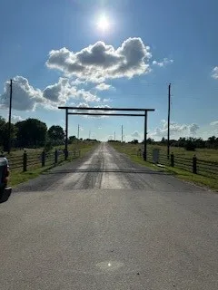 Gated entrance featuring a metal archway, paved driveway, and perimeter fencing