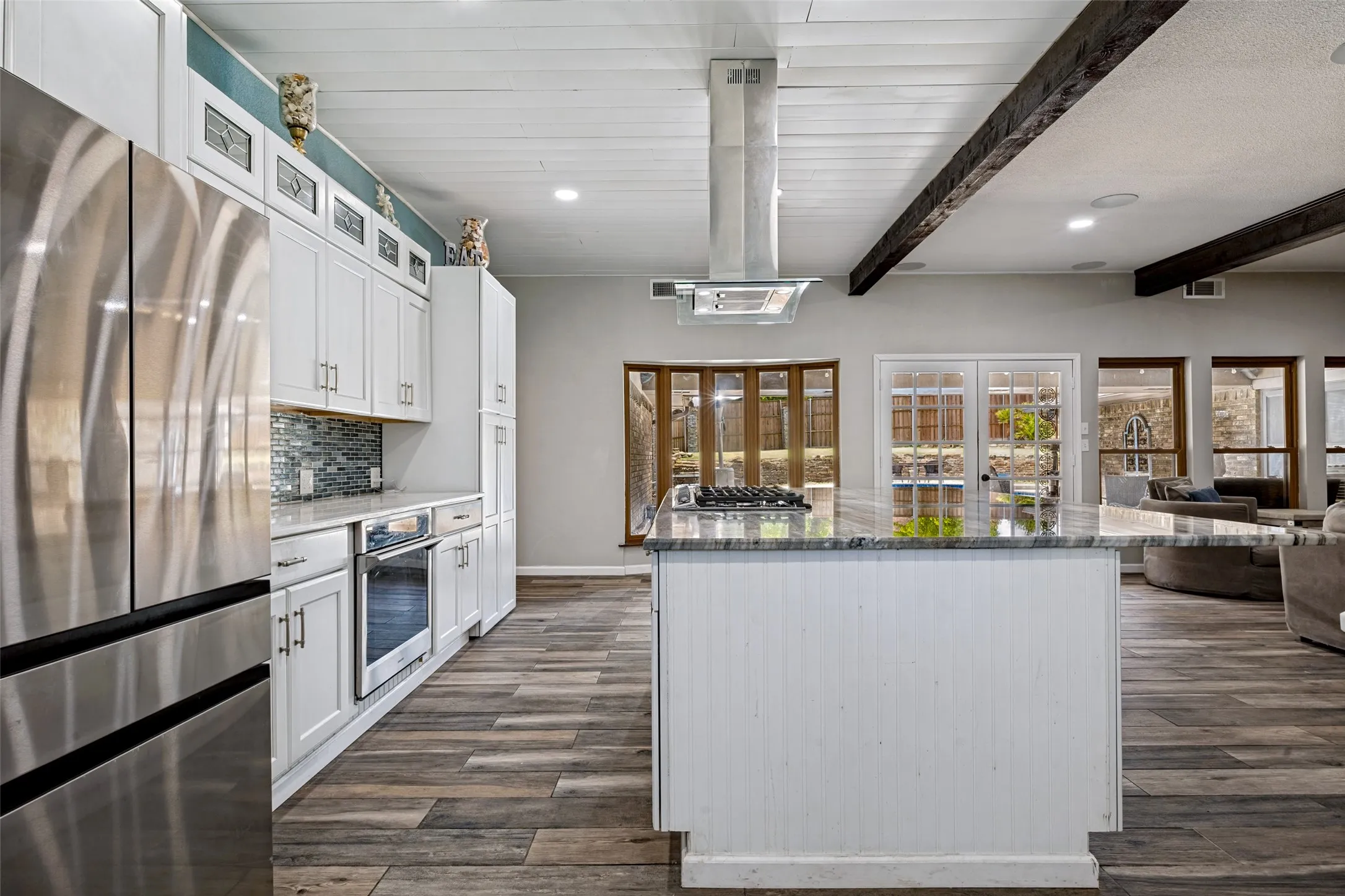 Kitchen featuring a central island with a stone countertop, white cabinetry, a stainless steel refrigerator, and porcelain ceramic wood-finish flooring