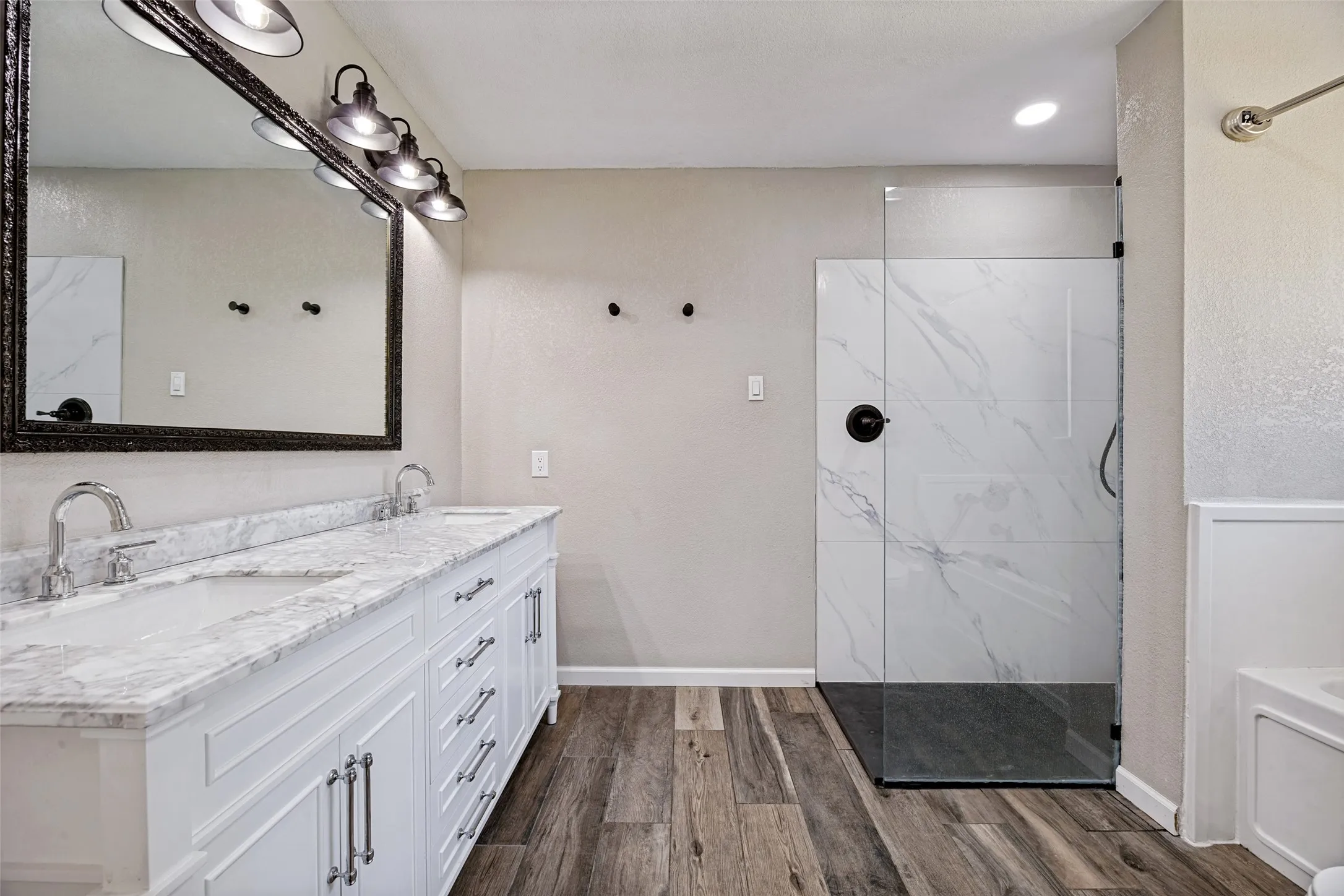 Double vanity with stone countertop and dual undermount sinks, featuring a large framed mirror with multi-bulb lighting