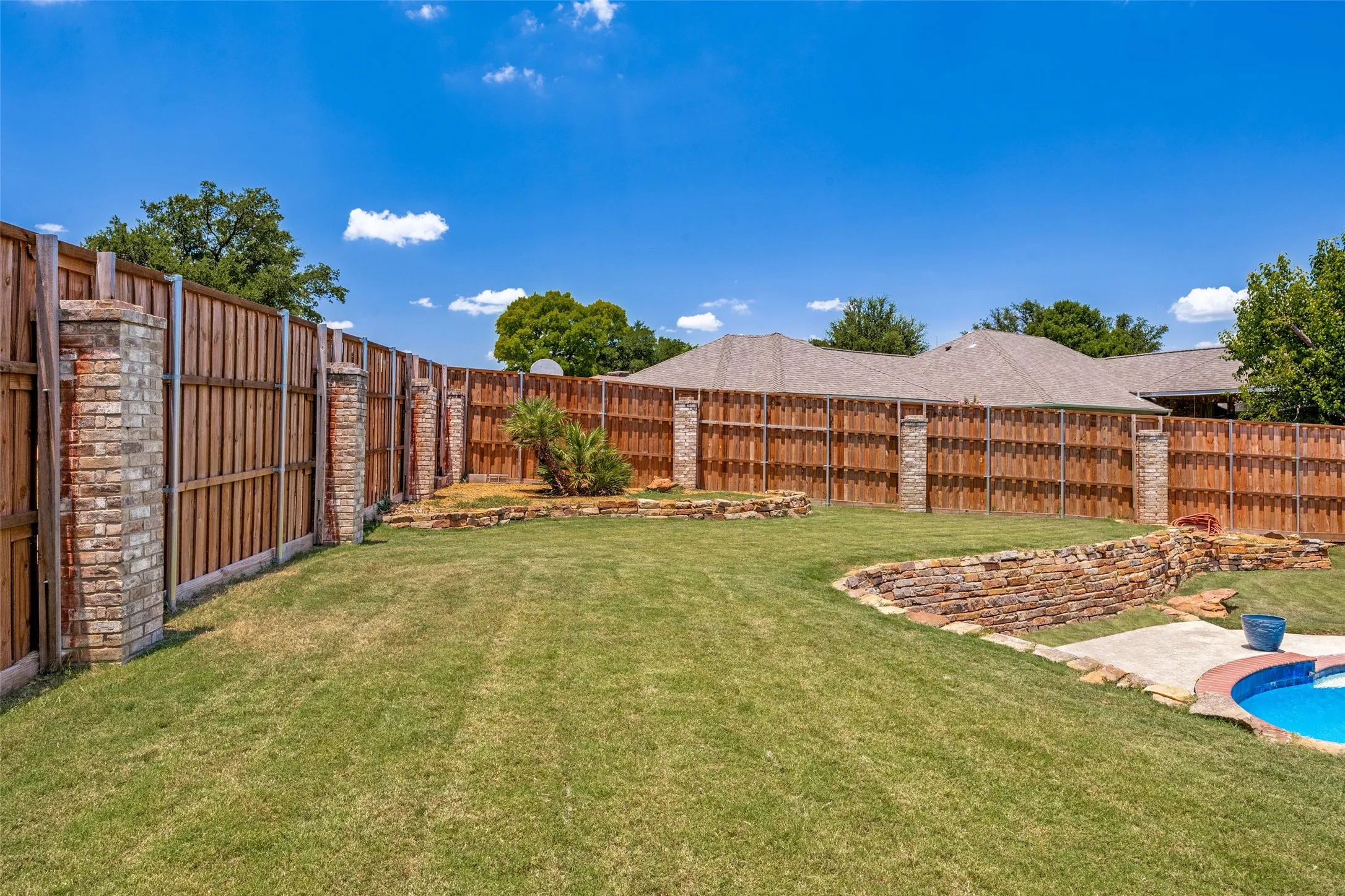 Expansive backyard featuring a manicured lawn, wood privacy fencing with brick pillars, and layered stone retaining walls
