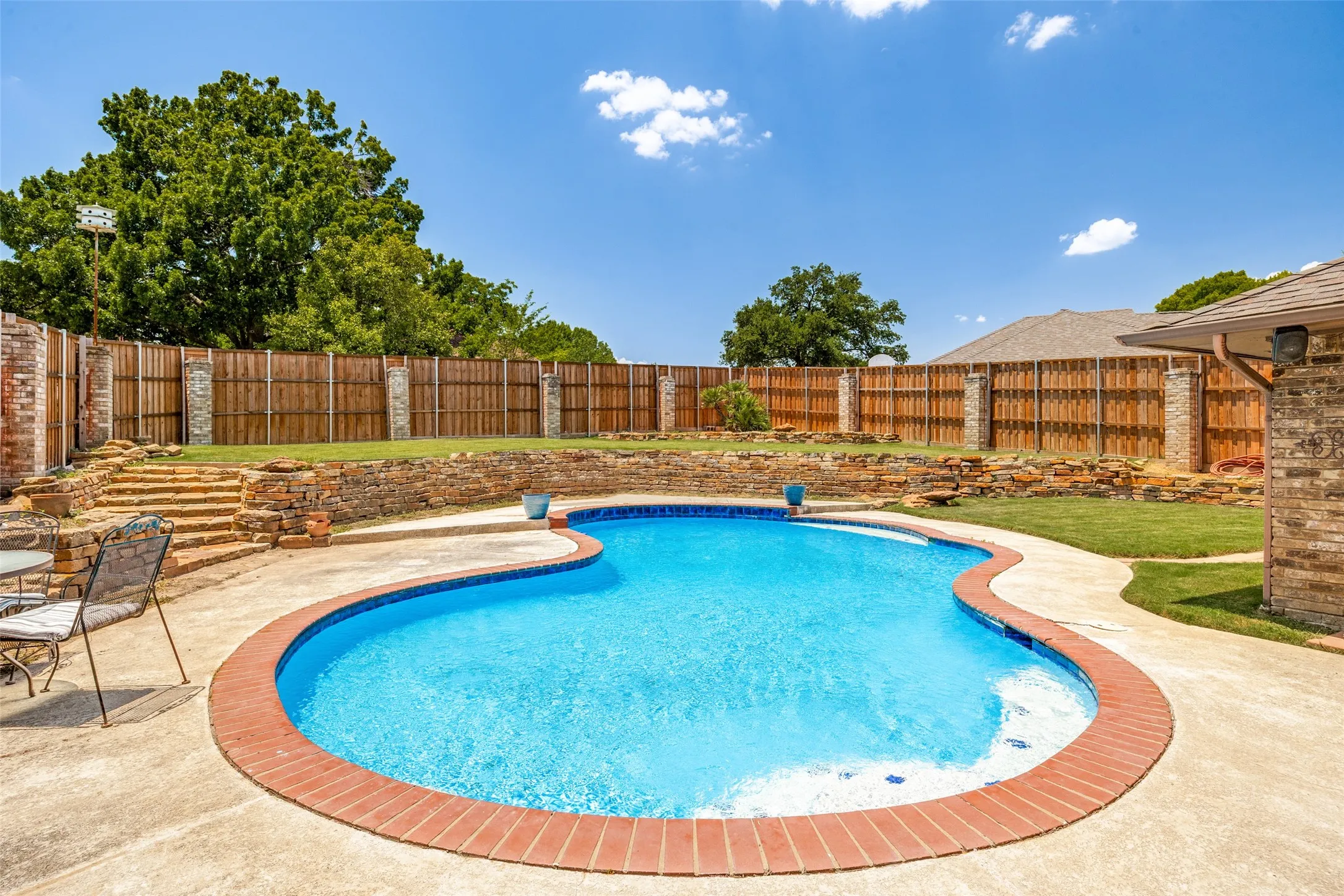 Freeform swimming pool with brick coping, surrounded by concrete decking