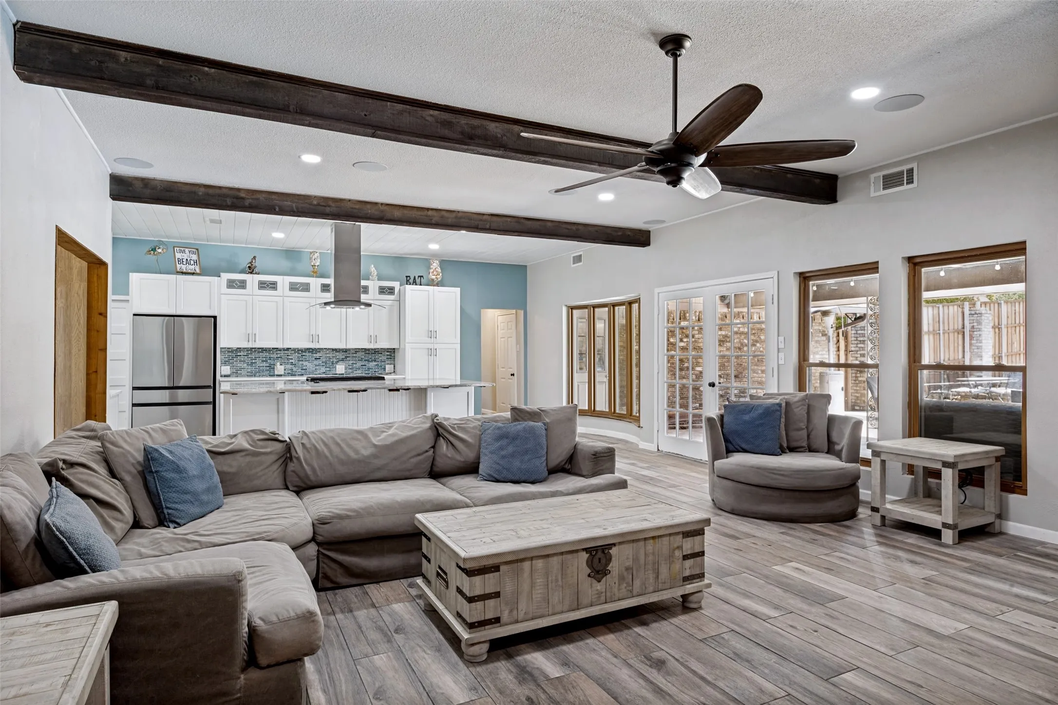Open-concept living space featuring porcelain ceramic wood-finish flooring, exposed ceiling beams, a ceiling fan, and recessed lighting