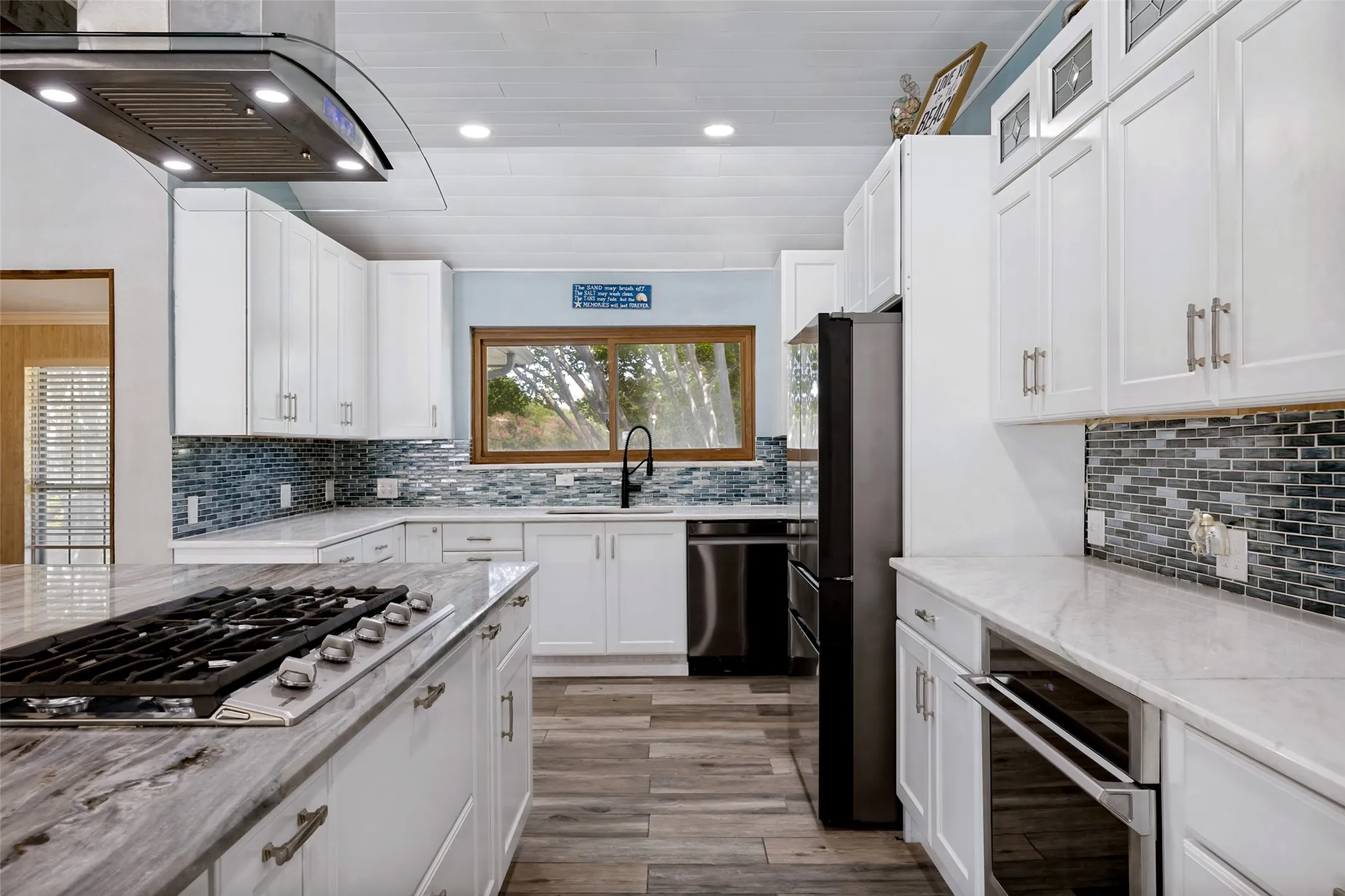 Kitchen featuring a large island with a built-in gas range, white shaker cabinetry, stainless steel appliances, and porcelain ceramic wood-finish flooring