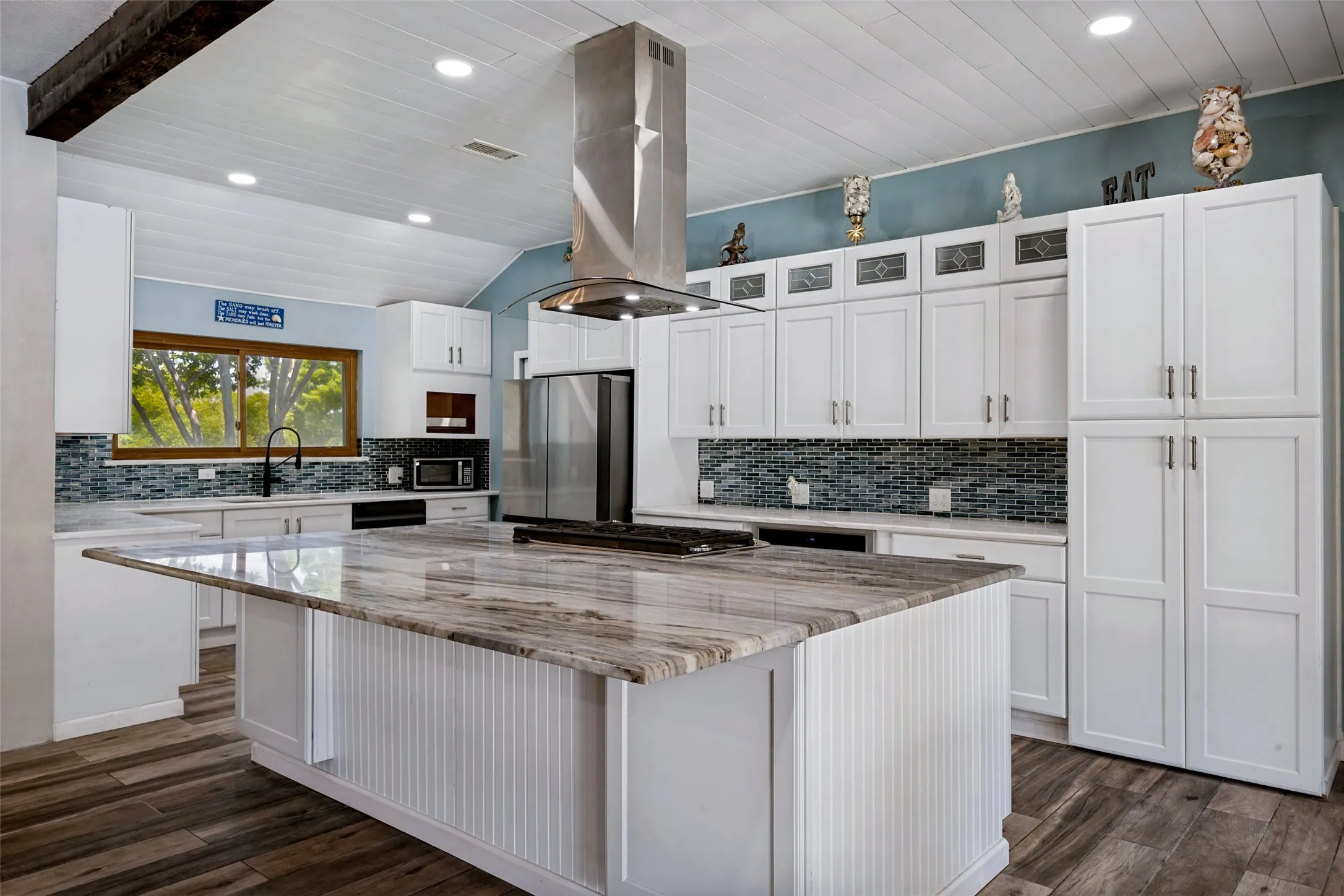Spacious kitchen featuring a large island with a natural stone countertop, stainless steel appliances, extensive white cabinetry, a mosaic tile backsplash, and porcelain ceramic wood-finish flooring