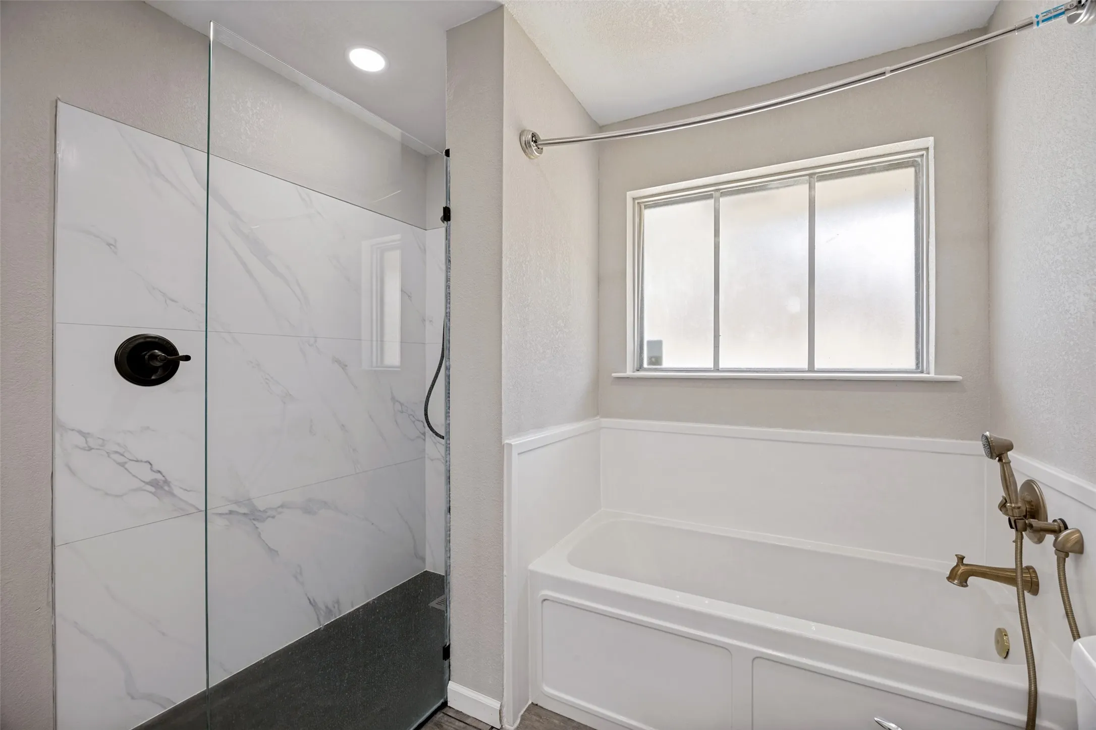 Walk-in shower with clear glass enclosure, marble-look tile surround, and matte black fixtures