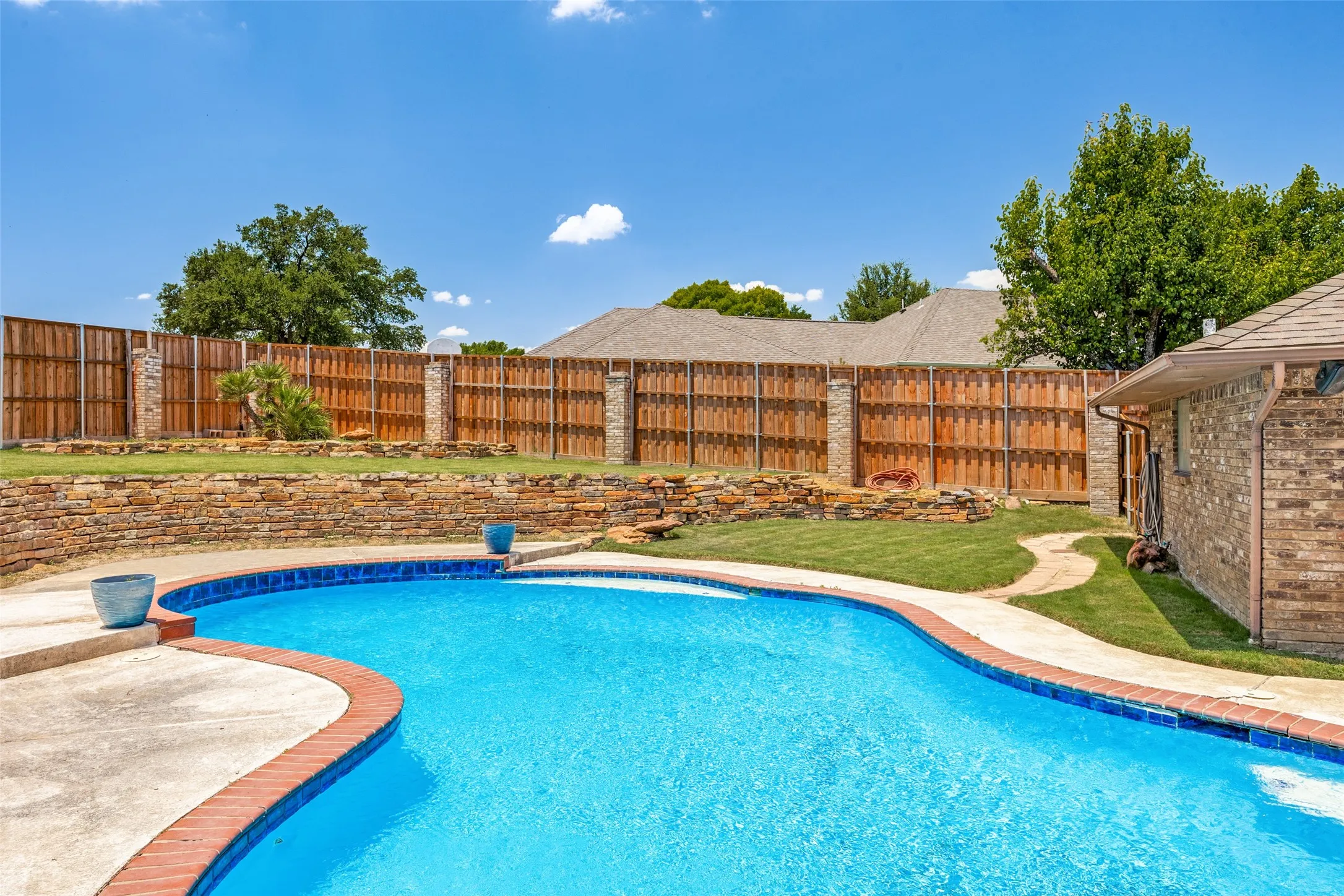 Inviting backyard featuring a freeform swimming pool with brick coping, concrete decking, and a brick-and-wood privacy fence