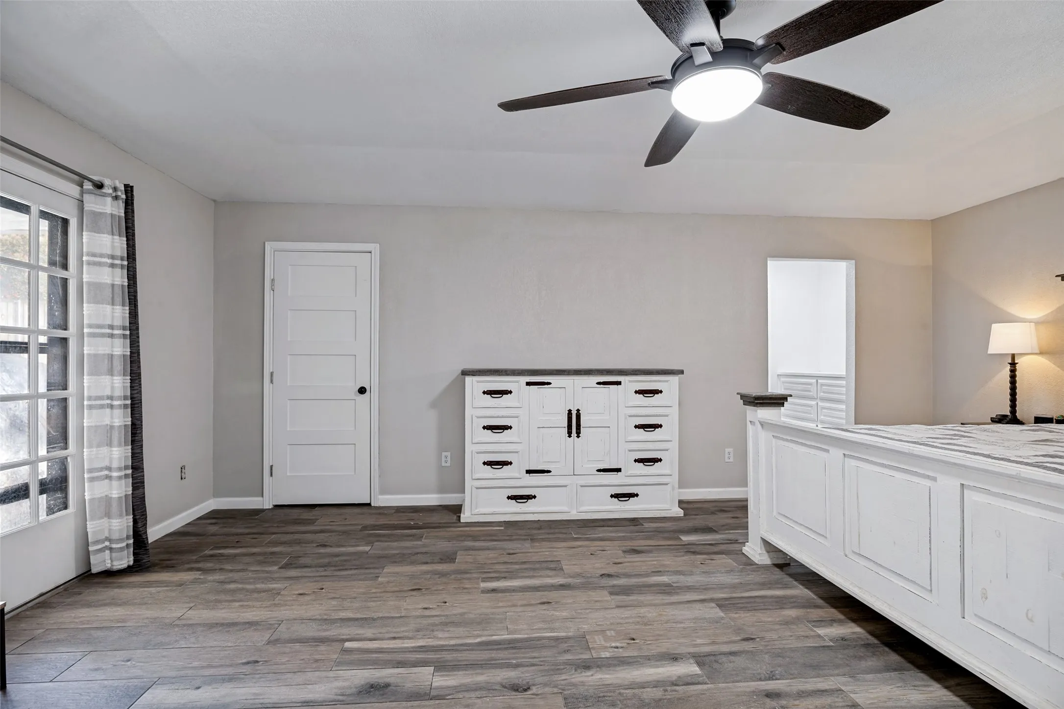 Spacious room featuring porcelain ceramic wood-finish flooring, a contemporary ceiling fan with integrated lighting, a white paneled door, and a glass-paned exterior door