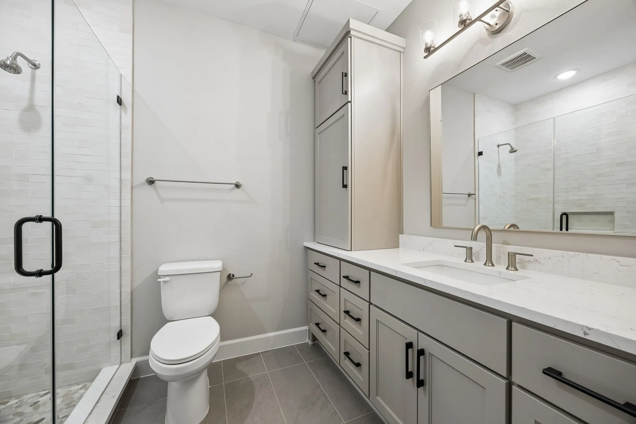 Bathroom featuring a glass-enclosed shower with subway tile surround, a single vanity with a white countertop and undermount sink, a tall linen cabinet, and a large mirror with vanity lighting