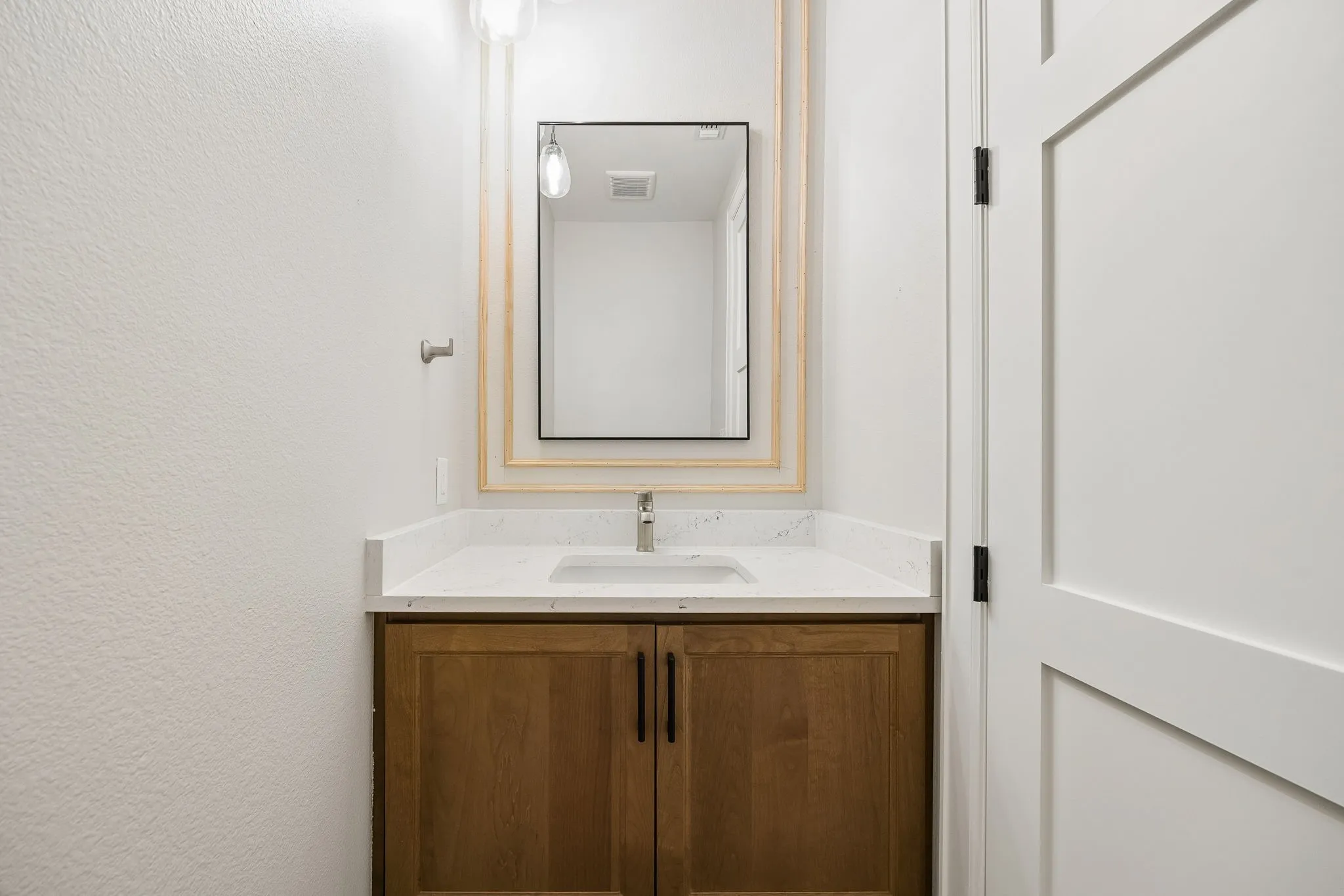 Vanity featuring a light wood-finish cabinet with black hardware, a light-toned countertop, and a rectangular undermount sink with a brushed nickel faucet