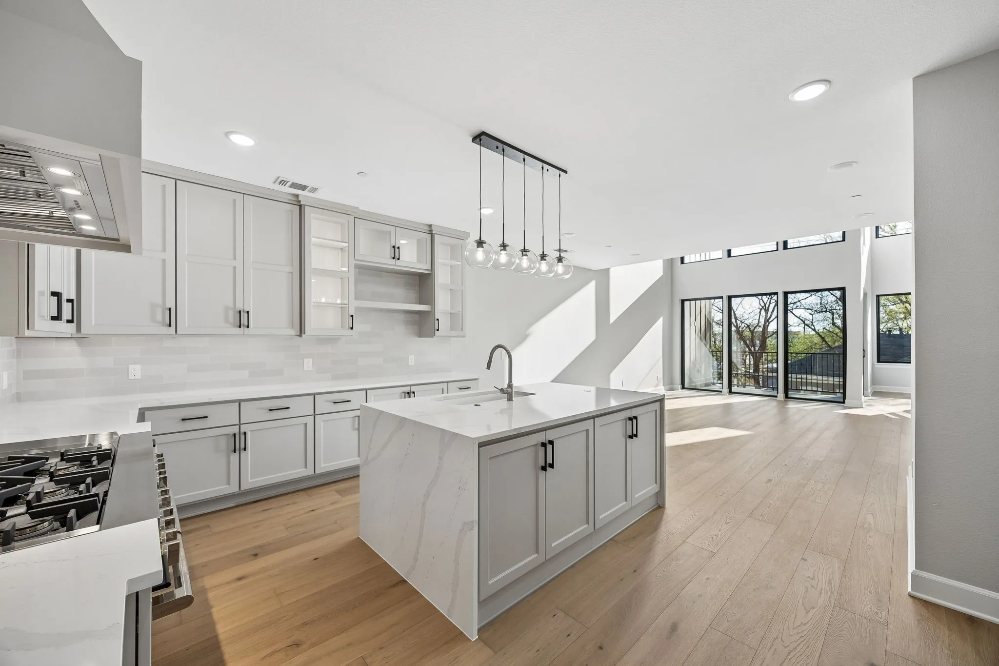 Contemporary kitchen featuring an island with a waterfall countertop, light wood-finish flooring, white shaker cabinetry with black hardware, a tiled backsplash, and recessed lighting