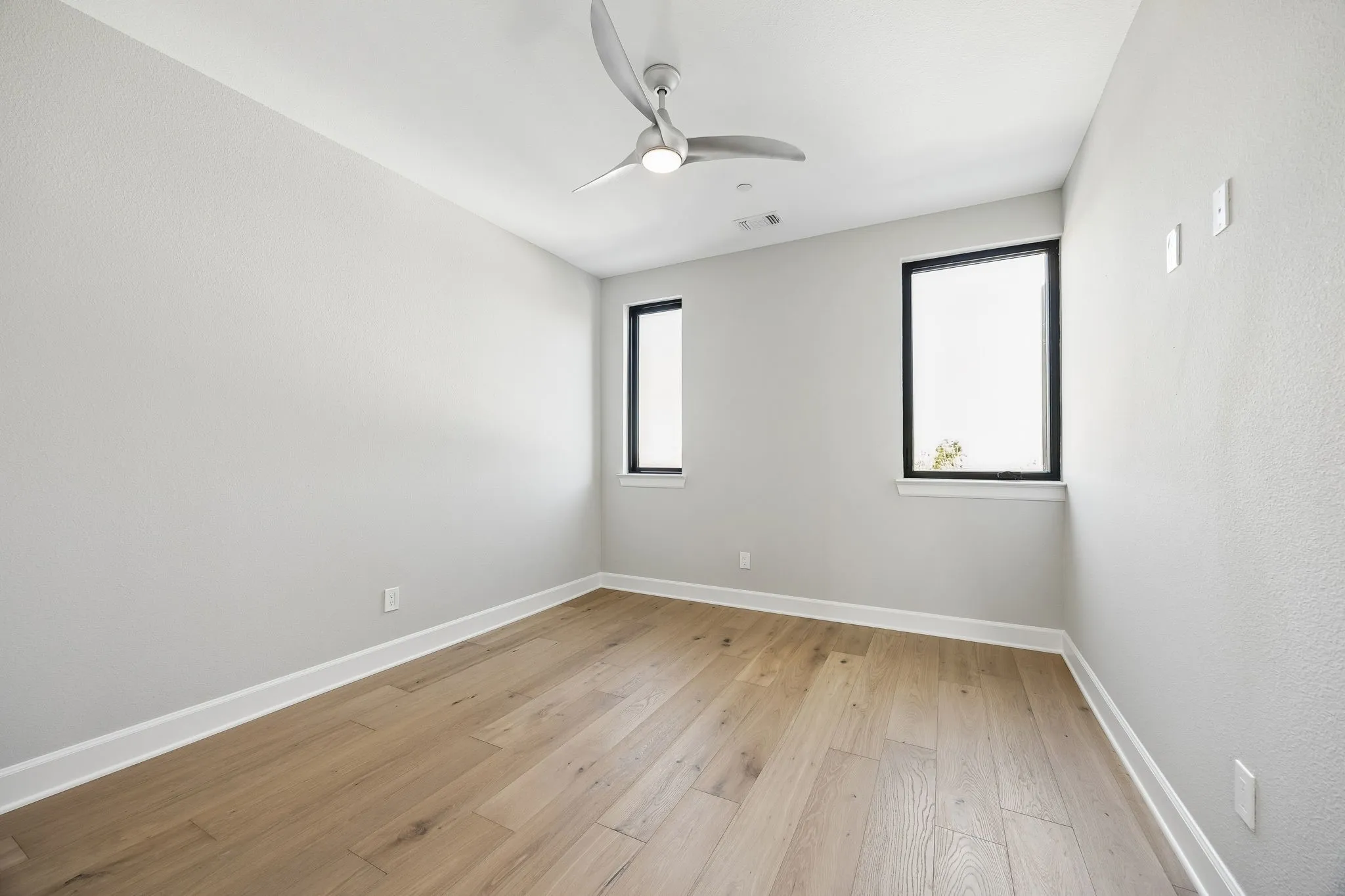 Room featuring wood-finish flooring, white baseboards, light grey walls, and a modern ceiling fan
