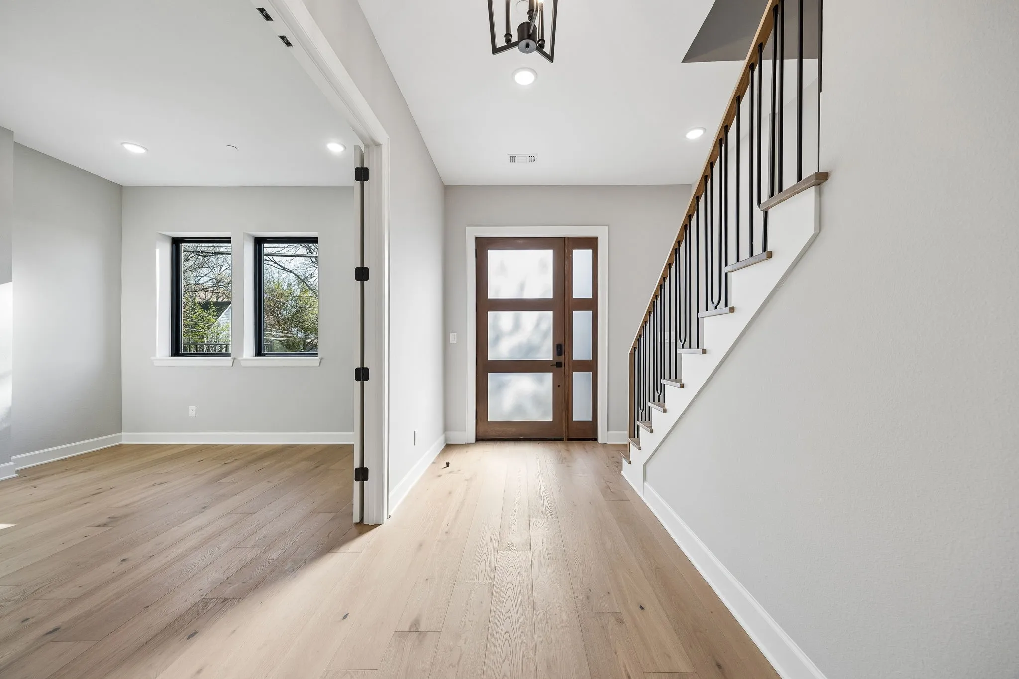 Foyer featuring a wood-panel entry door with frosted glass inserts, a contemporary staircase with black metal balusters and wood handrail, and light wood-finish flooring