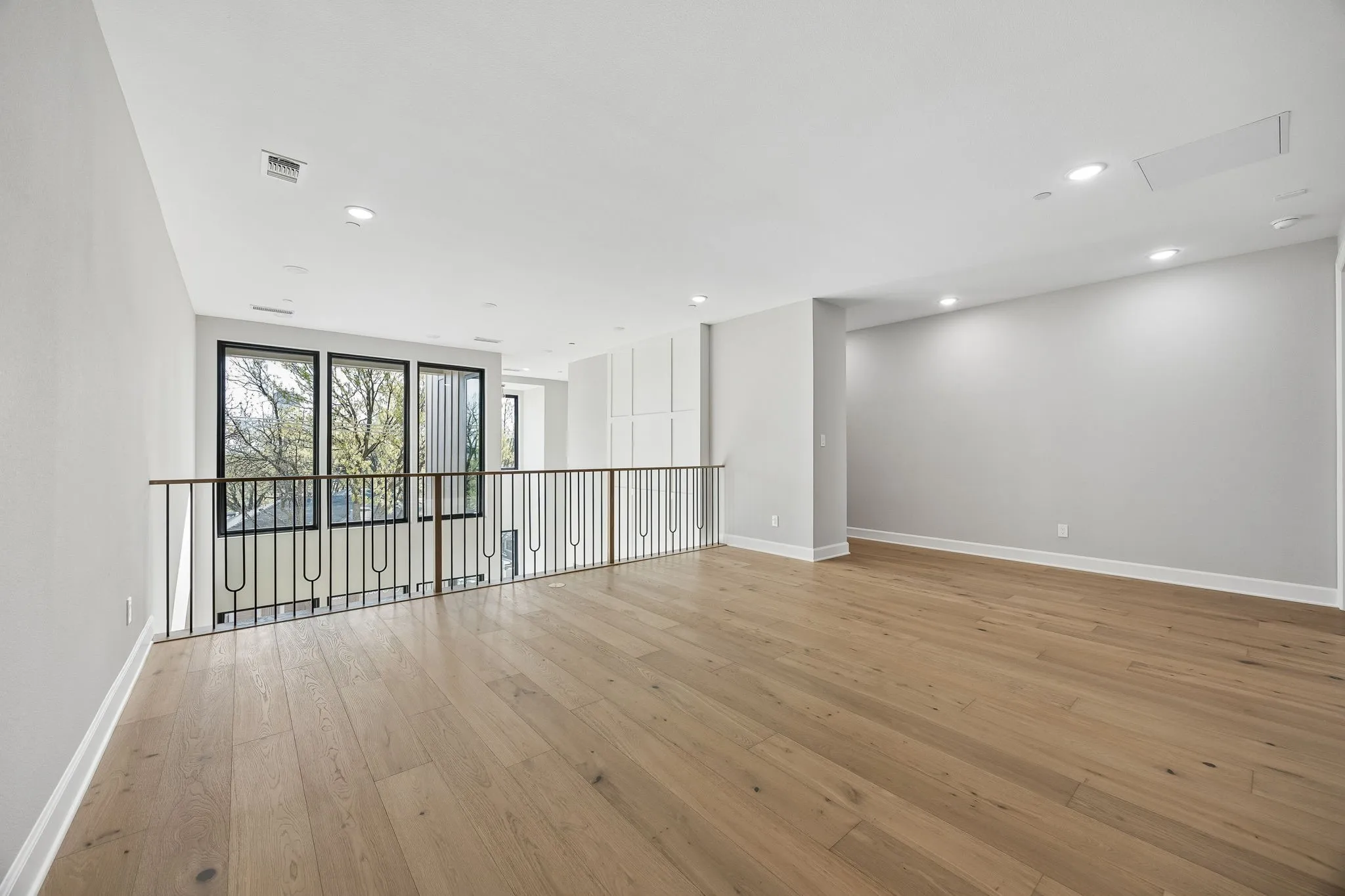 Open-concept loft space featuring wood-finish flooring, recessed lighting, and a contemporary metal​​‌​​​​‌​​‌‌​‌‌​​​‌‌​‌​‌​‌​​​‌​​ railing