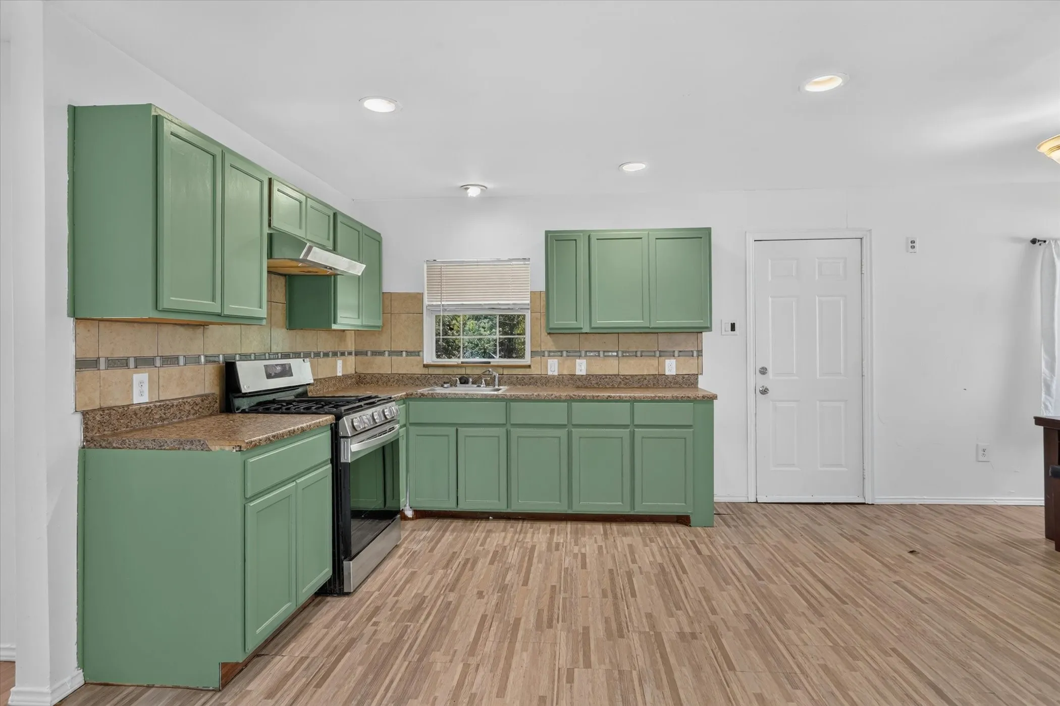 Kitchen featuring green cabinetry, tile backsplash, and gas range