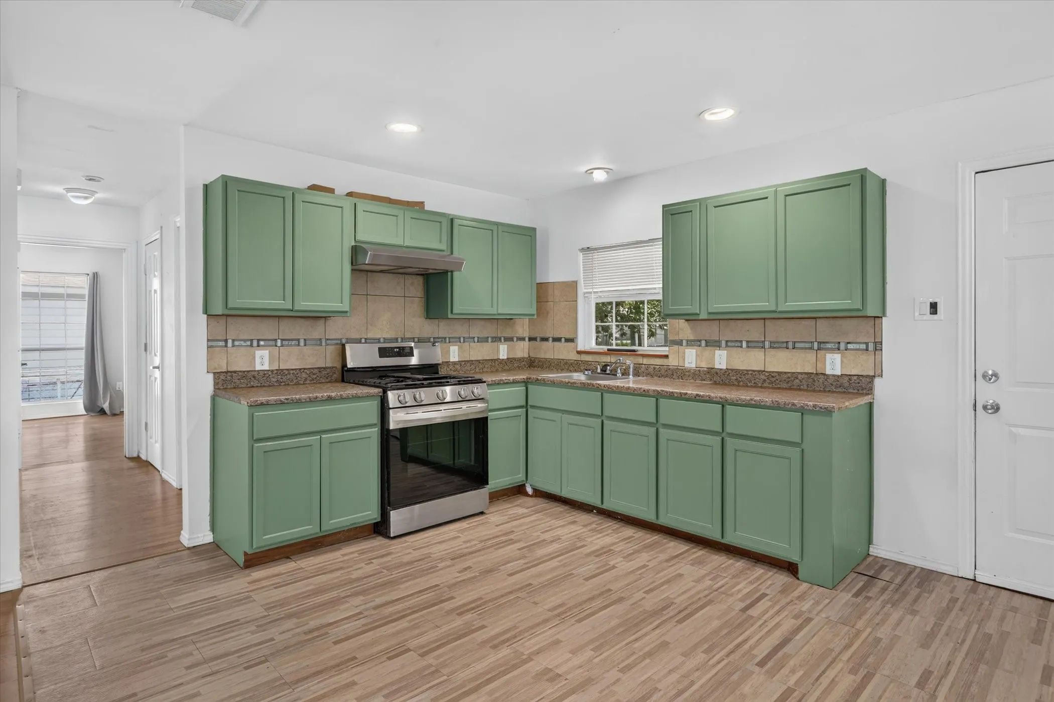 Kitchen featuring green cabinetry, gas range and a tile backsplash