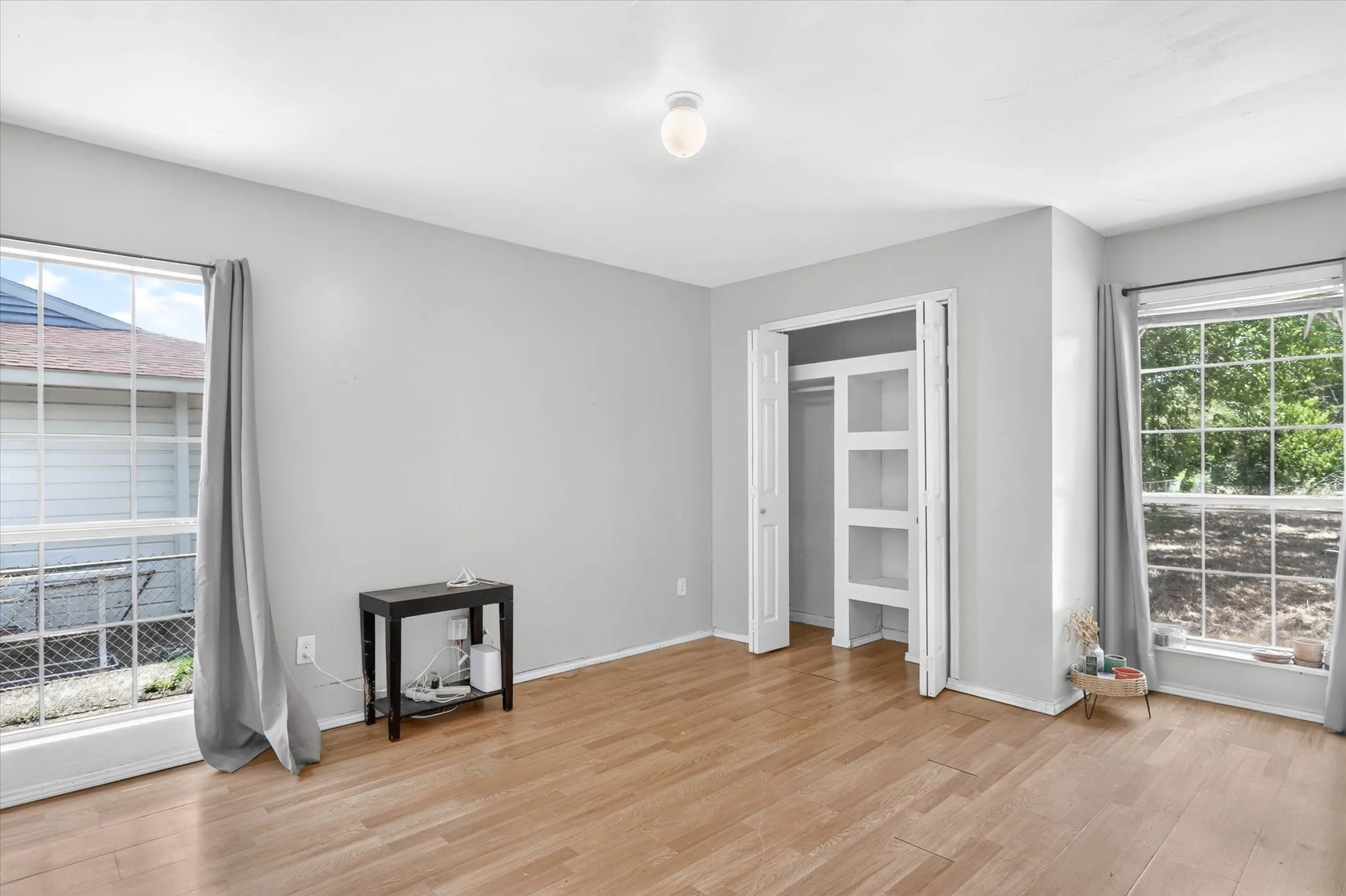 Spacious bedroom featuring light gray wall paint, two large windows, and a built-in closet with shelving