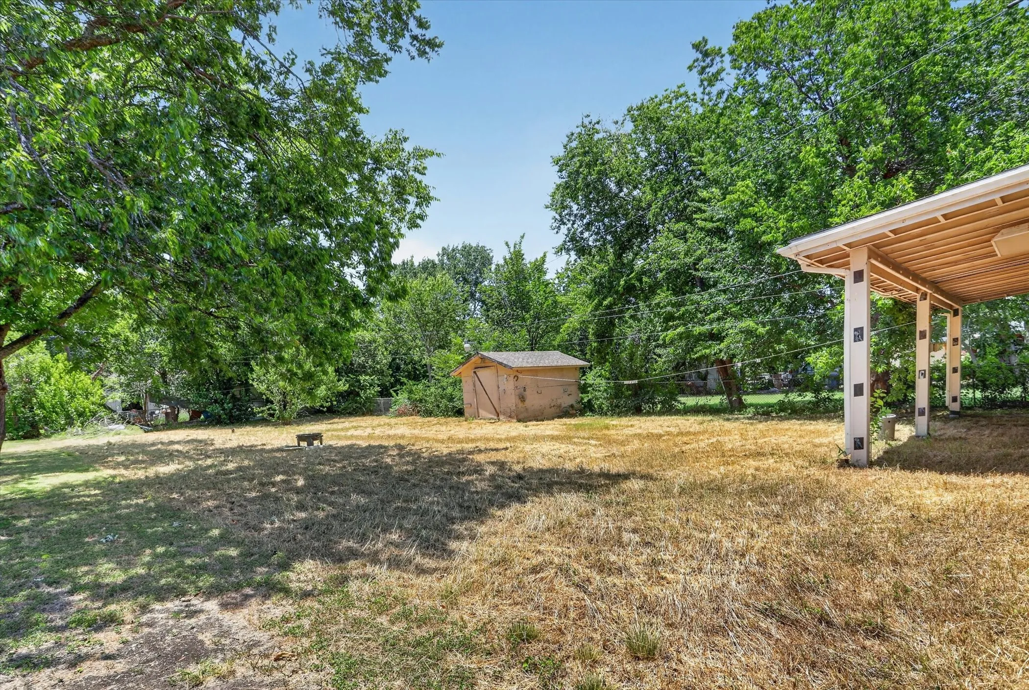 Expansive backyard featuring a covered patio, detached storage shed, and mature trees providing natural shade